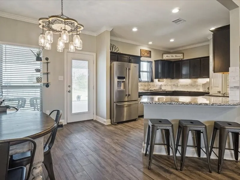 Wood-finish flooring, dark wood cabinetry, light-toned countertops, tile backsplash, and stainless steel appliances