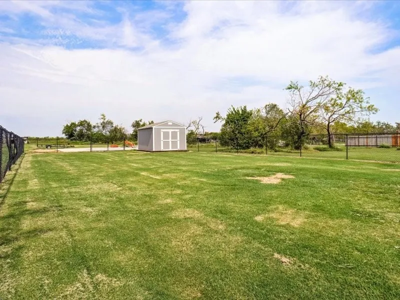 Expansive lawn area with perimeter fencing, a freestanding storage shed, and mature trees