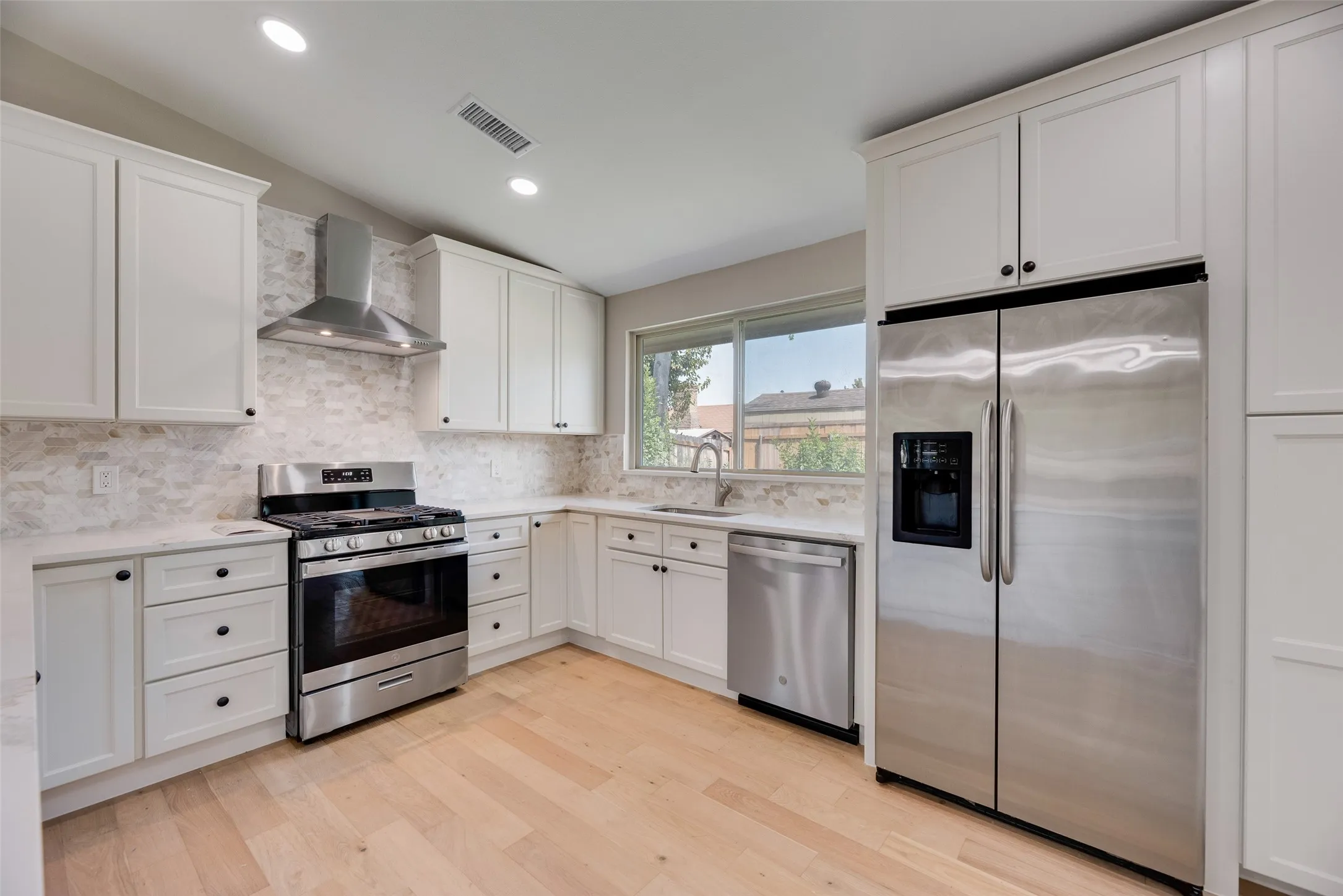 Kitchen featuring stainless steel appliances, white cabinets, wall chimney range hood, decorative backsplash, and recessed lighting