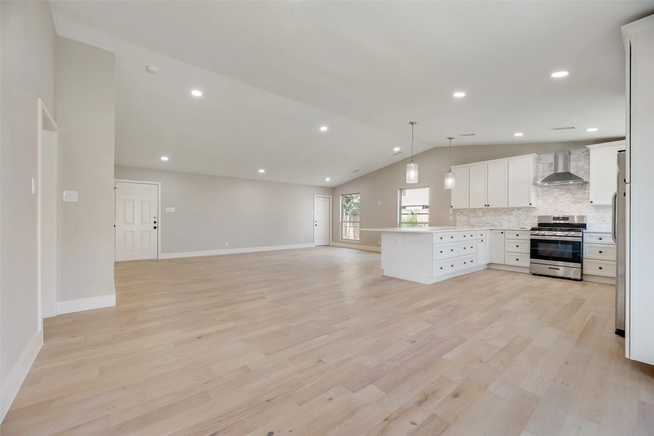 Kitchen featuring white cabinets, open floor plan, a peninsula, stainless steel appliances, and pendant lighting