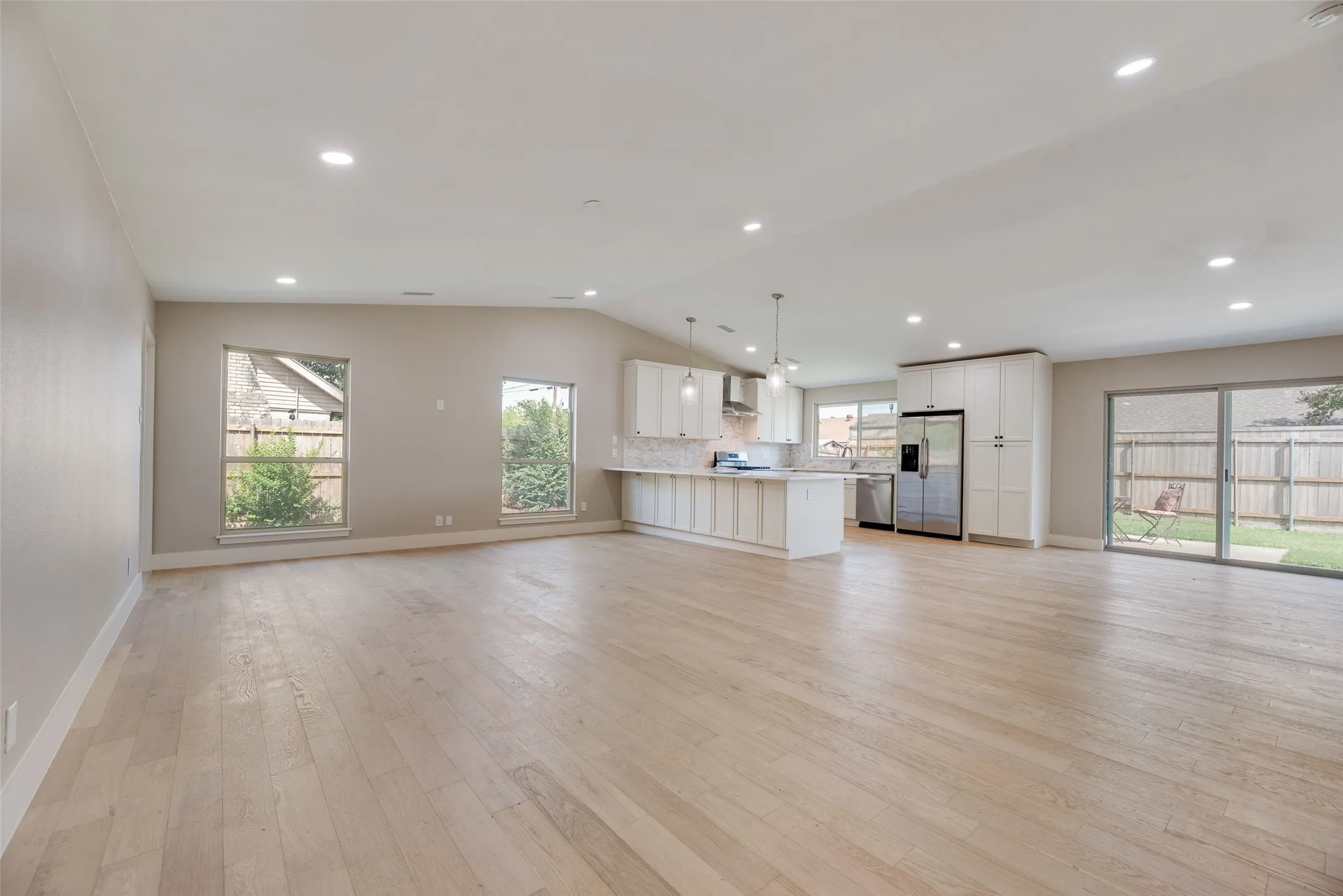 Open layout of living, dining, and kitchen with light wood finished floors, recessed lighting, oversized windows and lofted ceiling