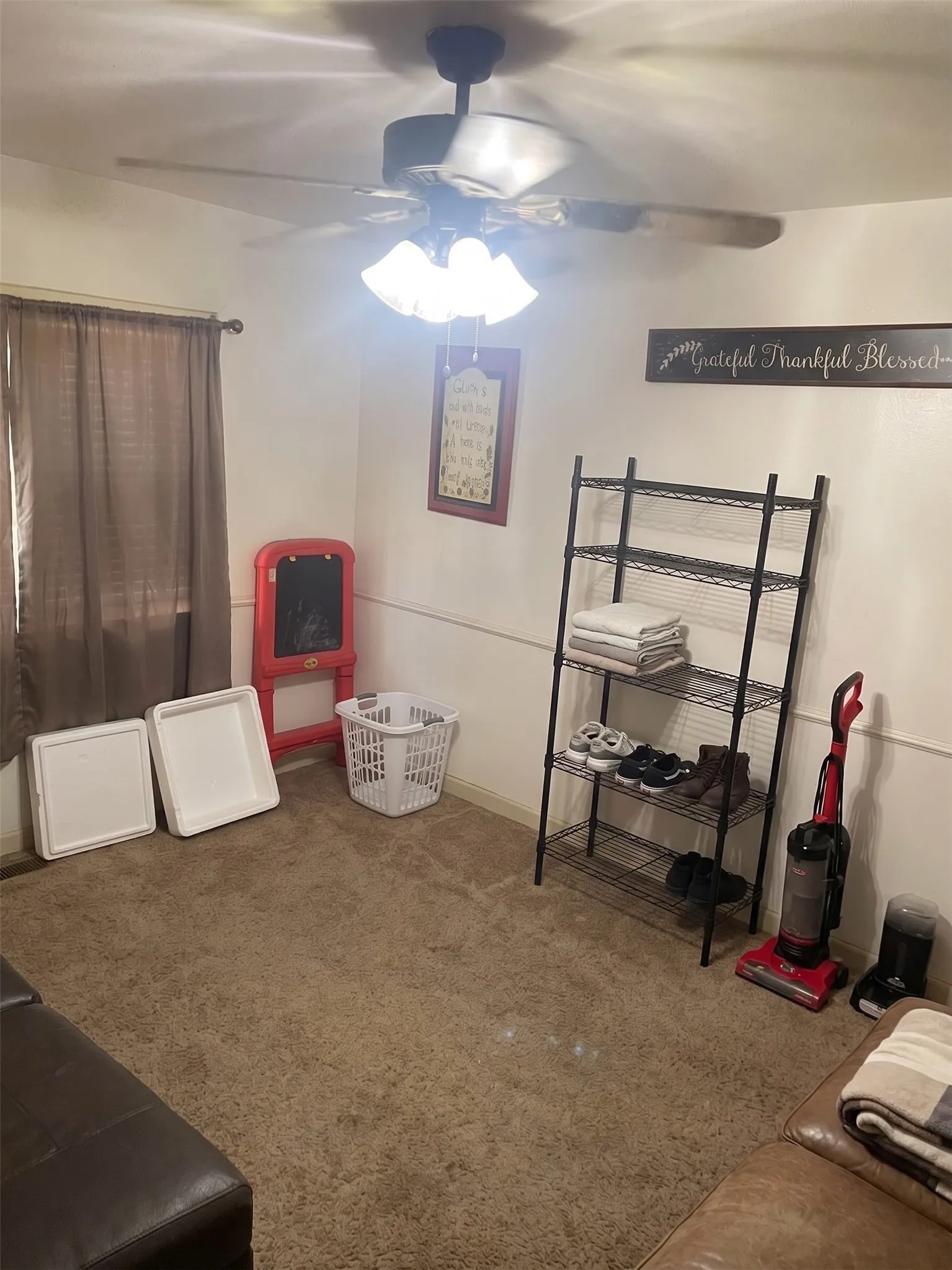 Spacious living room area featuring carpeted flooring, central ceiling fan, and open floor space.