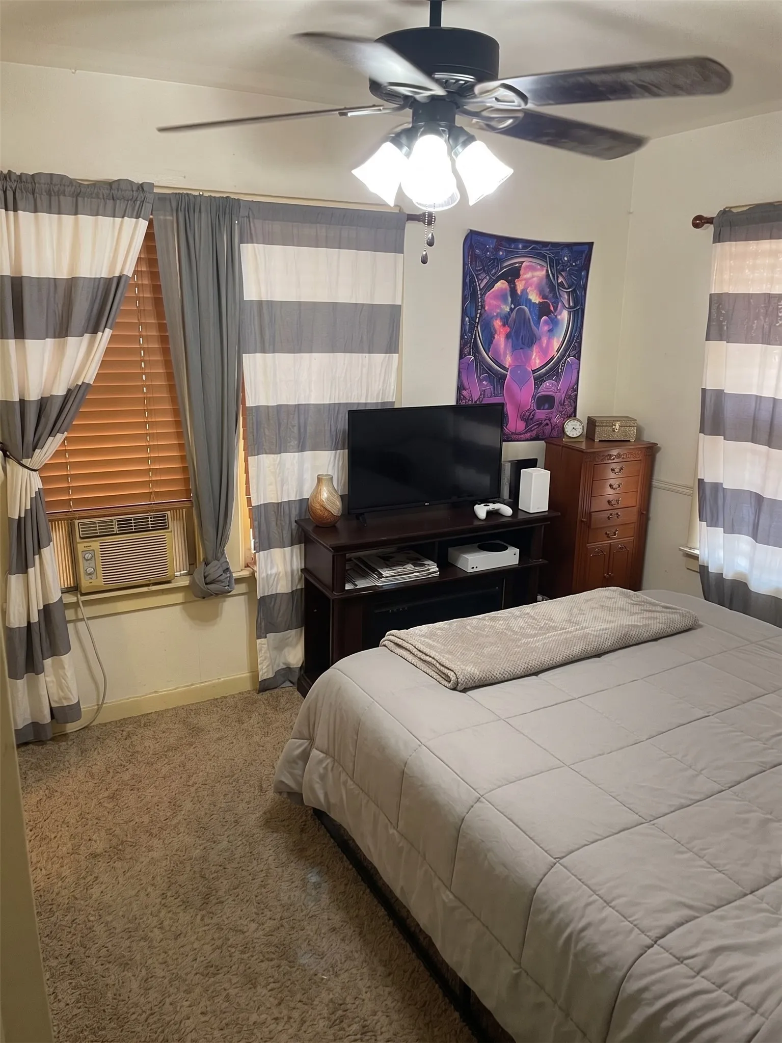 Comfortable bedroom layout equipped with carpet flooring, overhead ceiling fan, and bright window lighting.