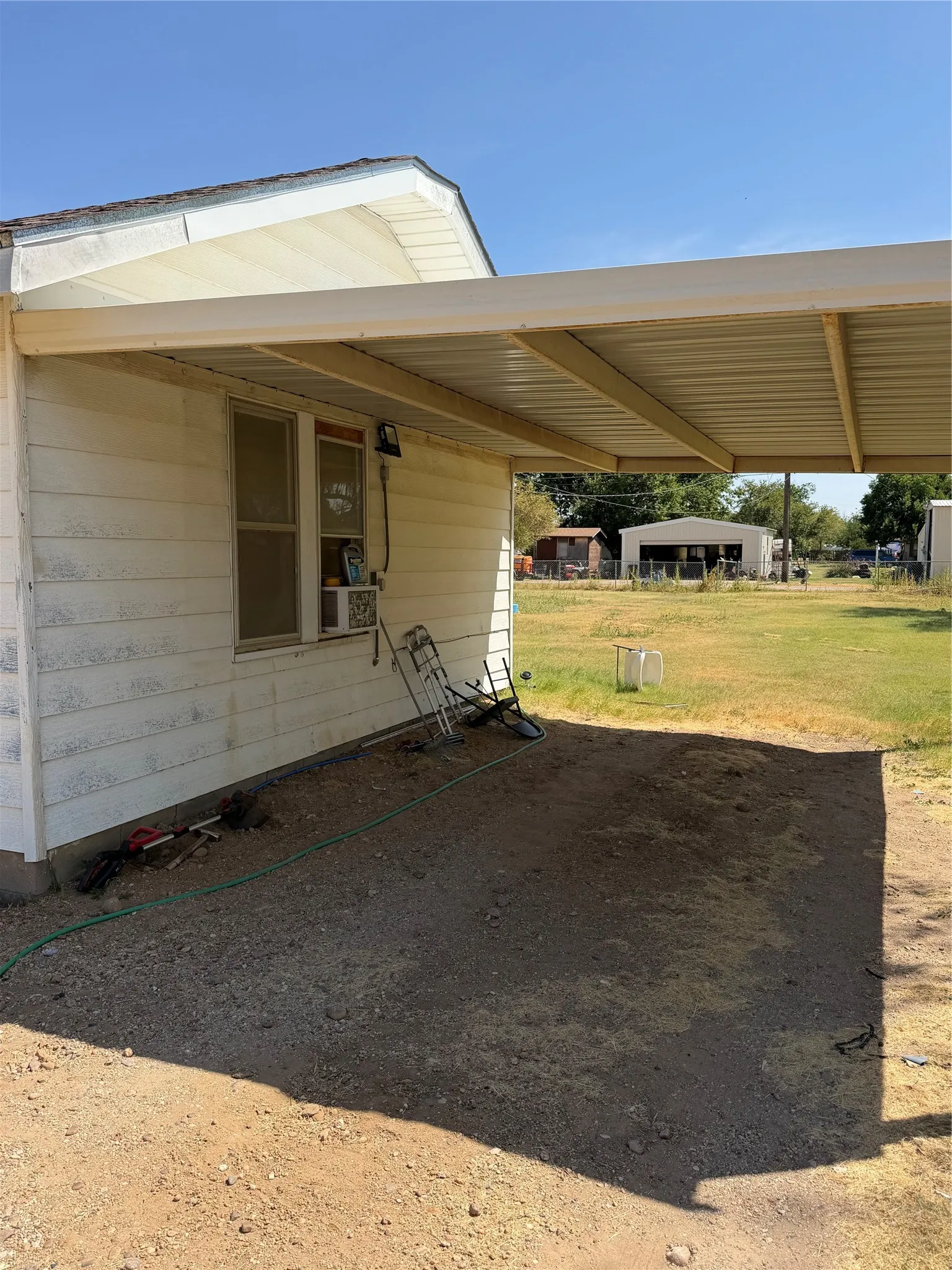Covered carport structure providing shaded parking and paved concrete pad.