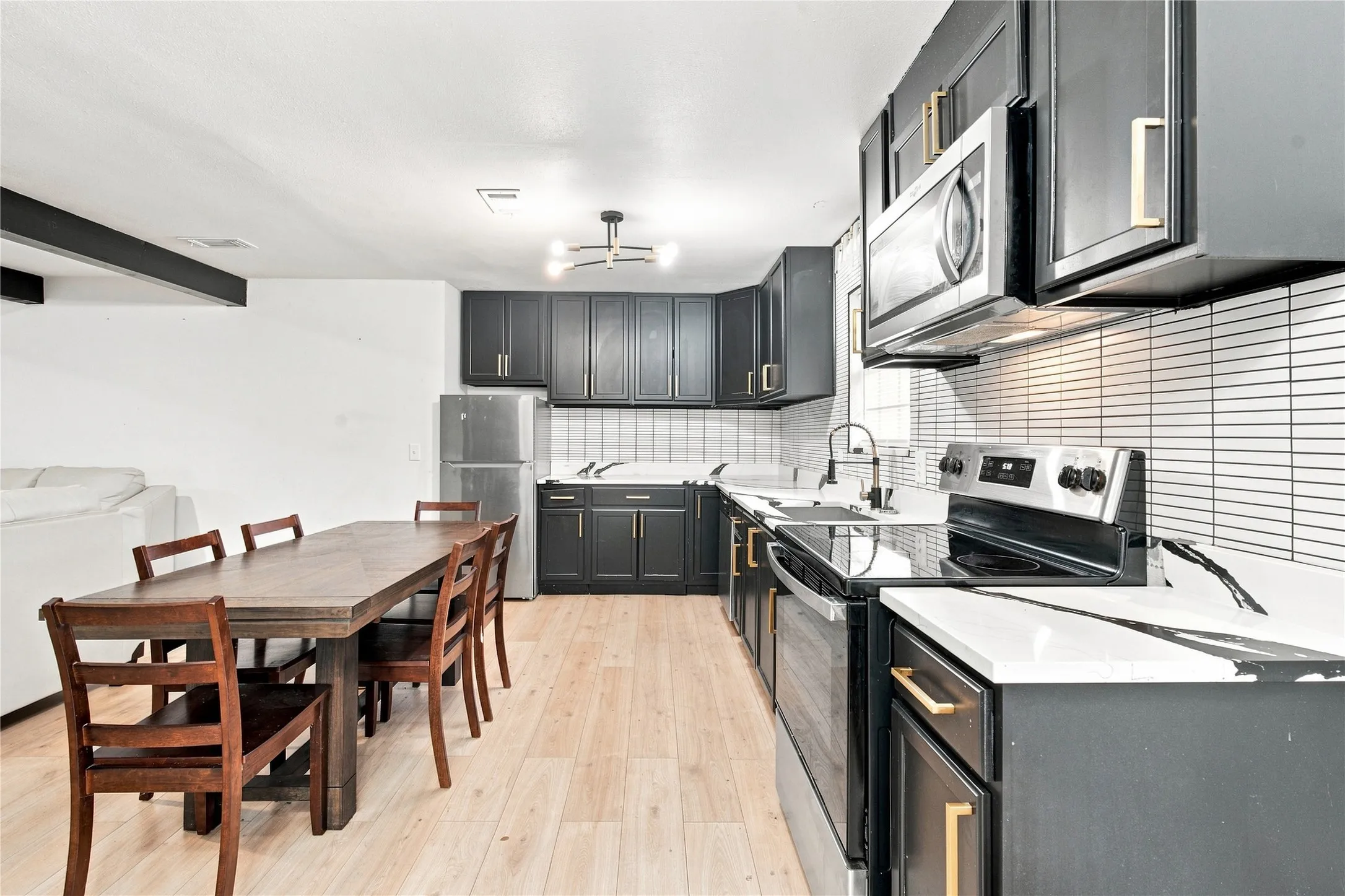 Kitchen featuring dark cabinetry, stainless steel appliances, light countertops, and a subway tile backsplash