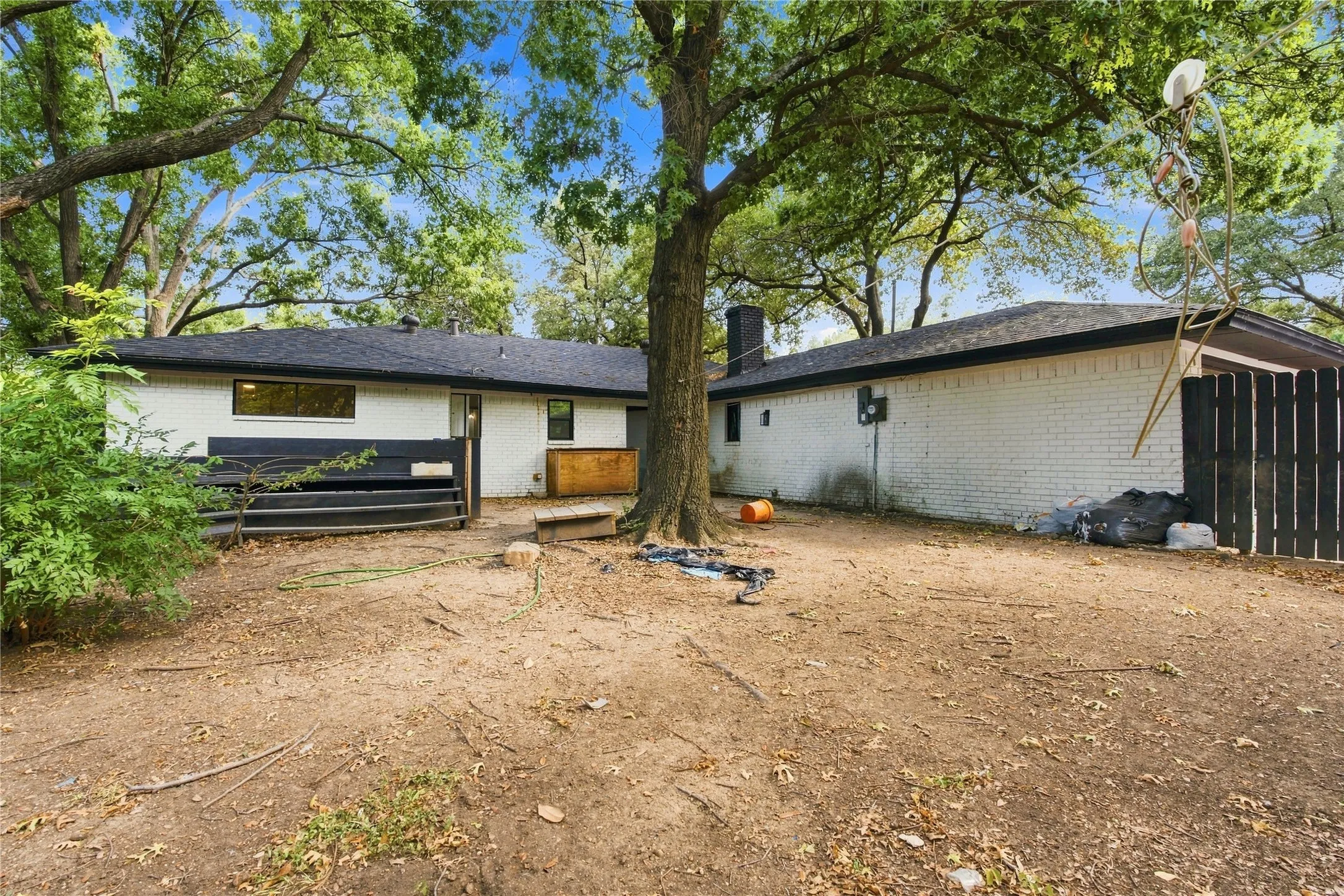Backyard featuring mature trees providing natural canopy, white brick exterior, black trim, and a black privacy fence