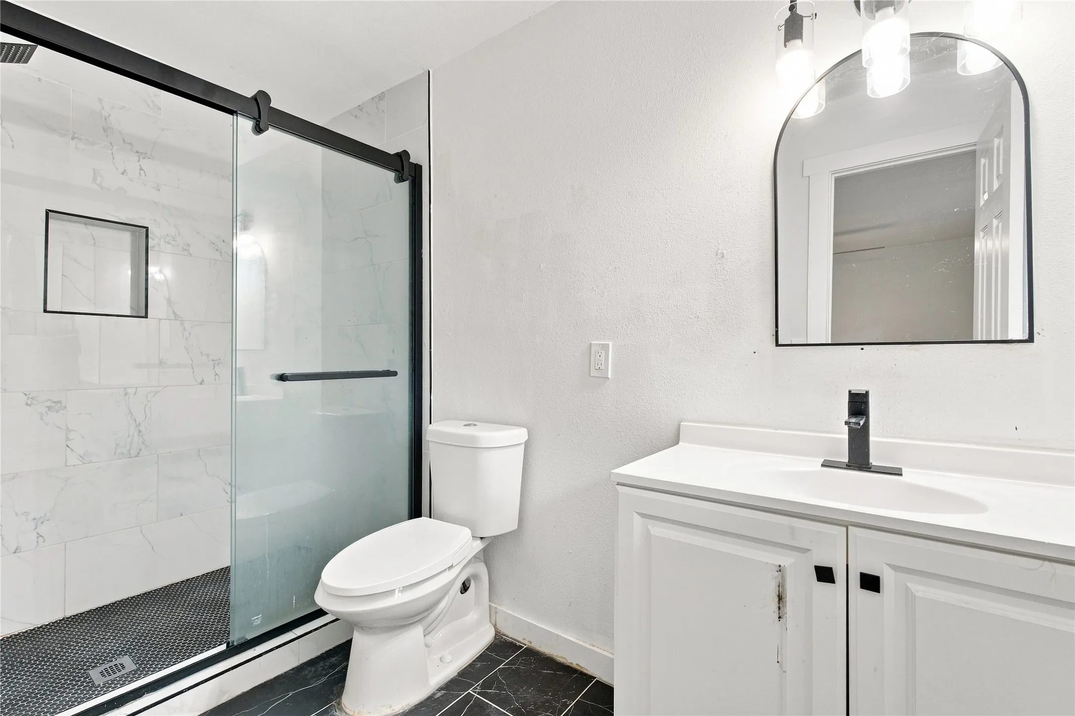 Frameless glass shower enclosure with black hardware, rainfall showerhead, and a built-in shower niche