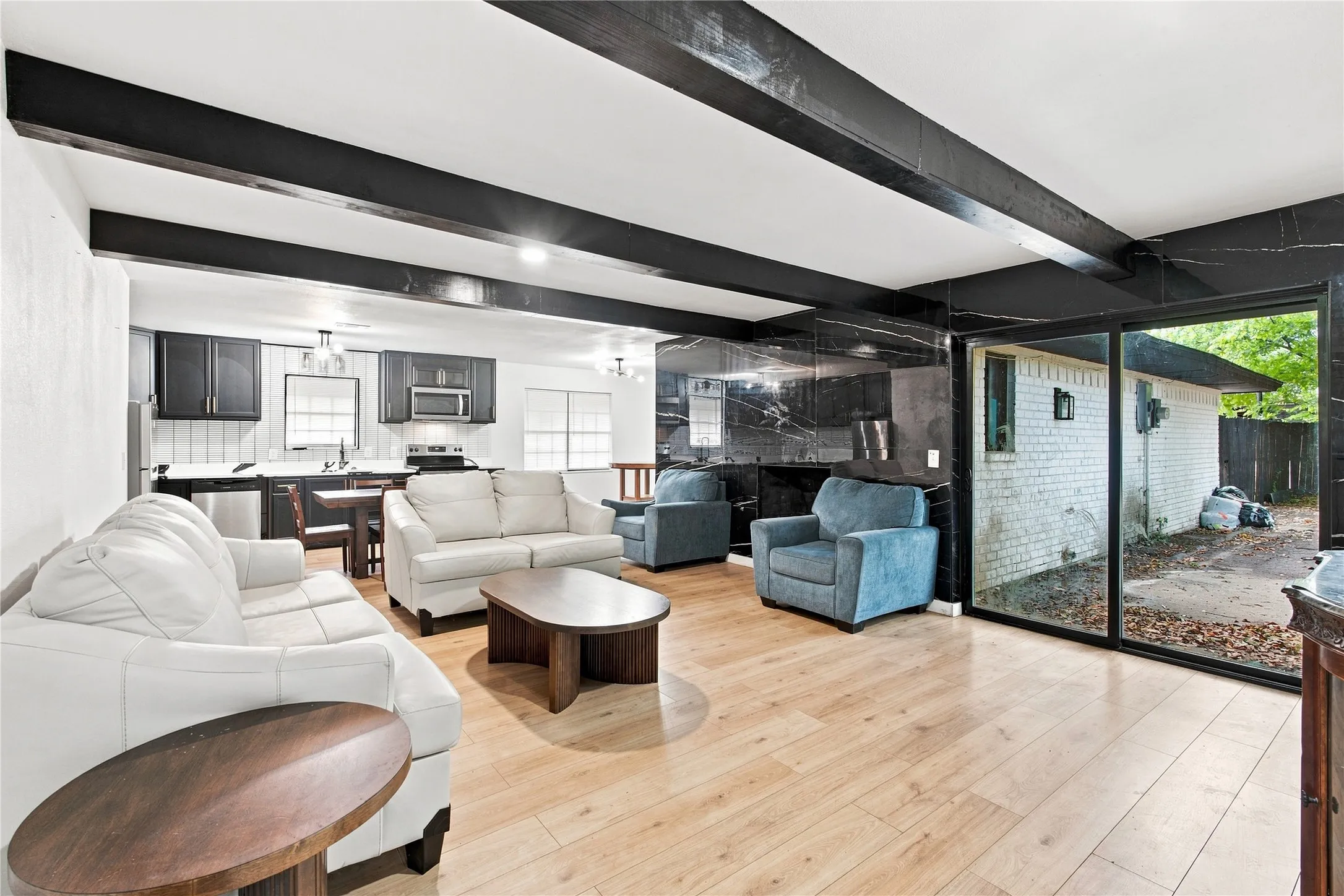 Hardwood-style flooring, exposed ceiling beams, built-in kitchen cabinetry, stainless steel appliances, and sliding glass doors