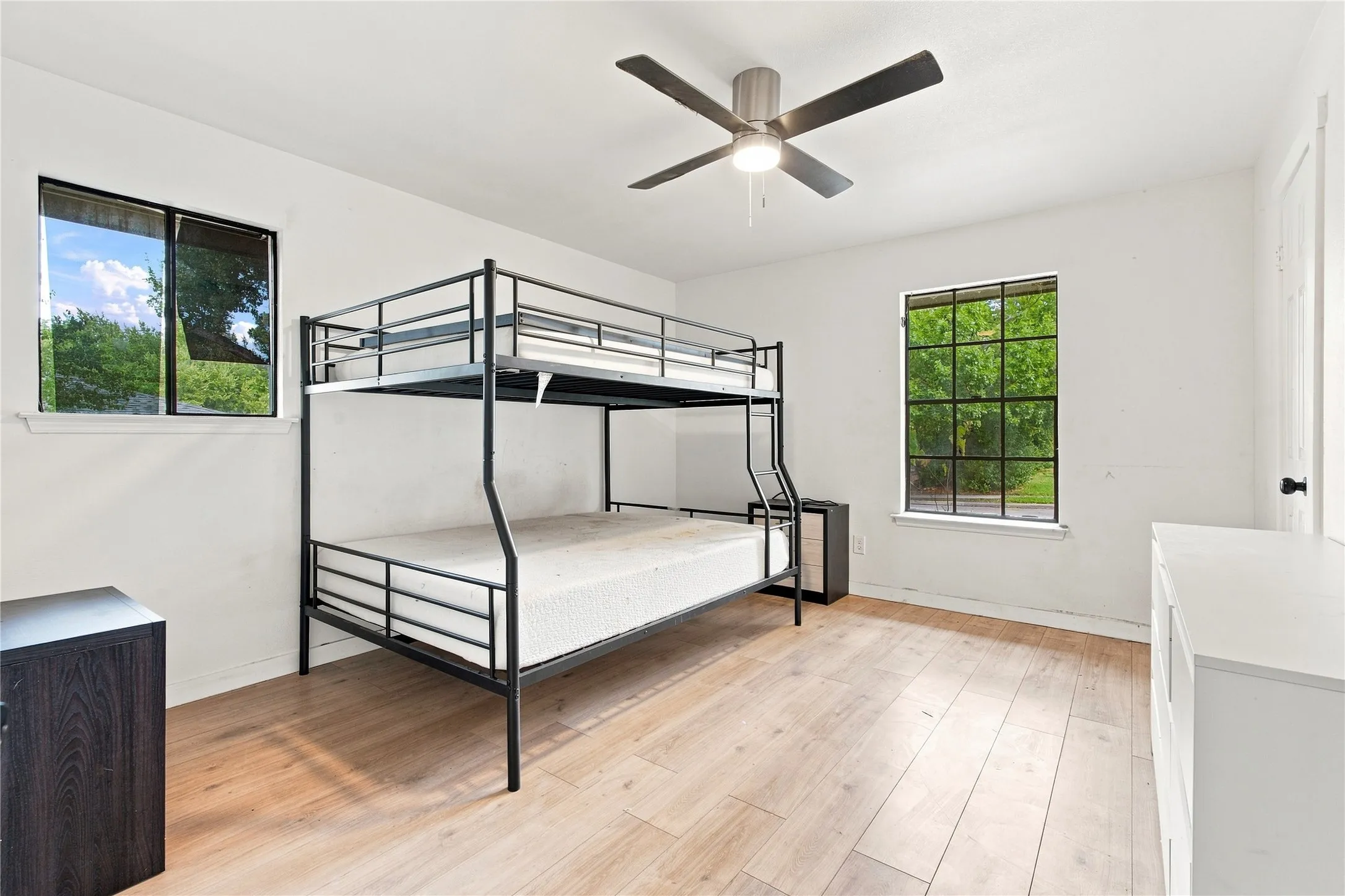 Spacious room featuring light wood-finish flooring, a ceiling fan, and two large windows