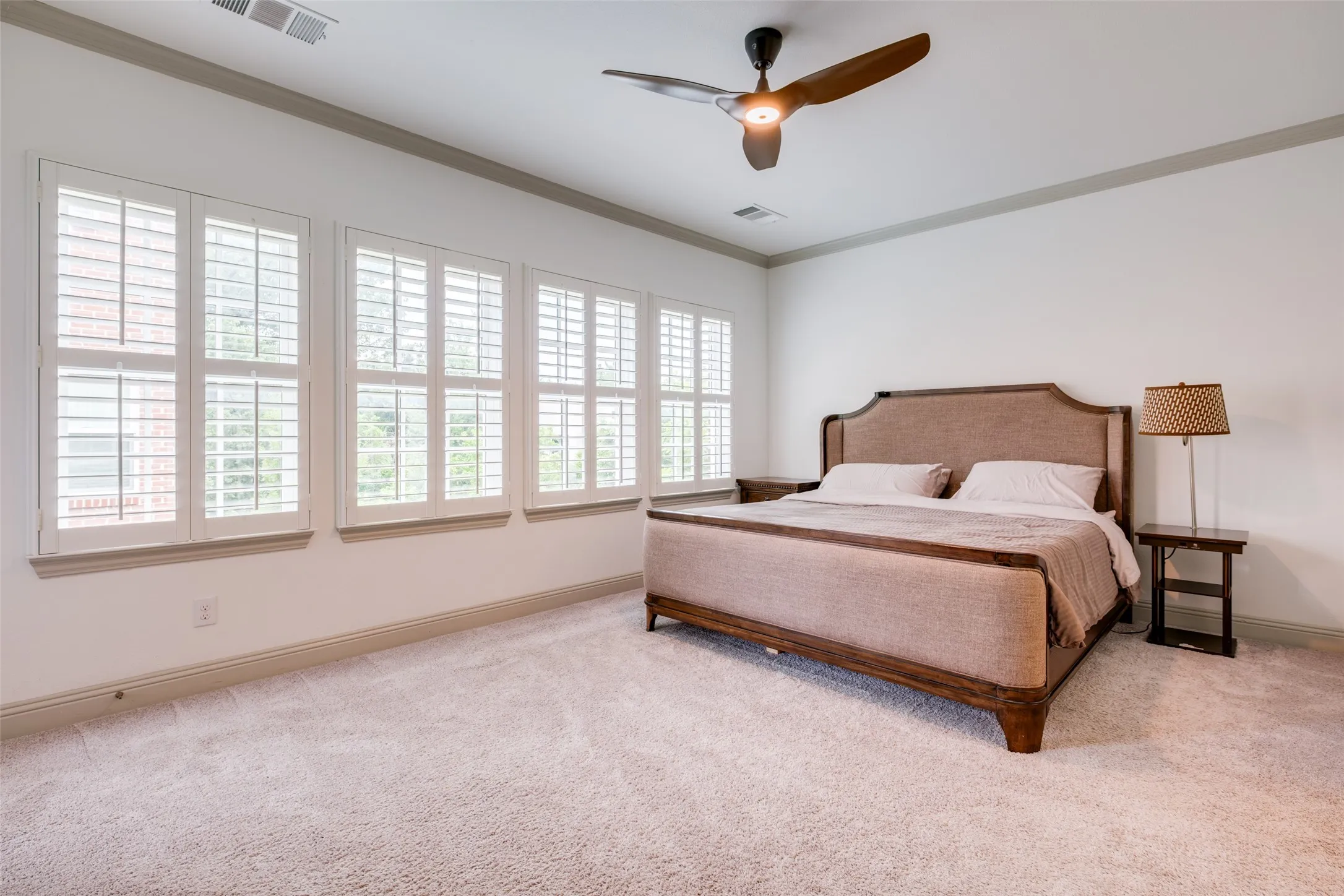 Spacious primary bedroom with lots of windows, crown molding and ceiling fan