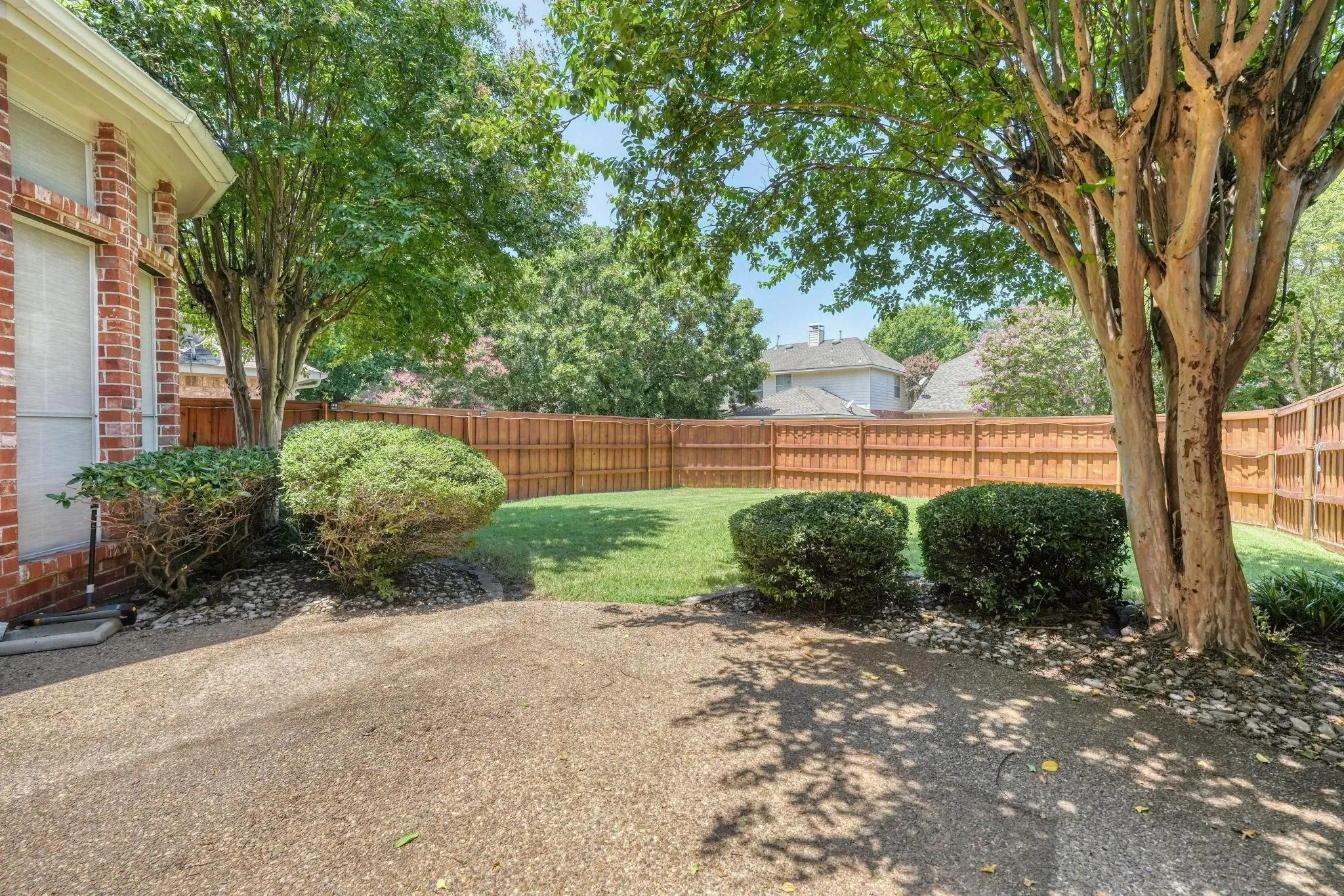 Expansive backyard featuring a manicured lawn, established privacy fence, mature trees, and a brick exterior