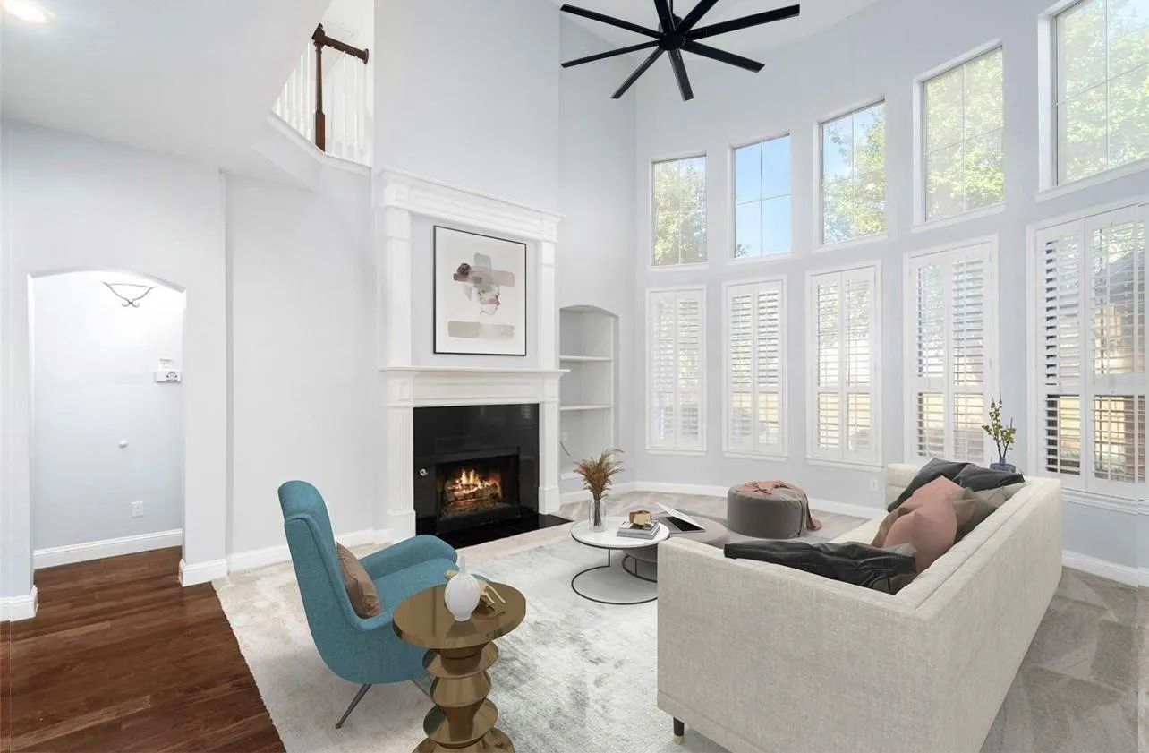 Two-story living area with high ceilings, a fireplace with a decorative mantel, multiple large windows, and an arched entry