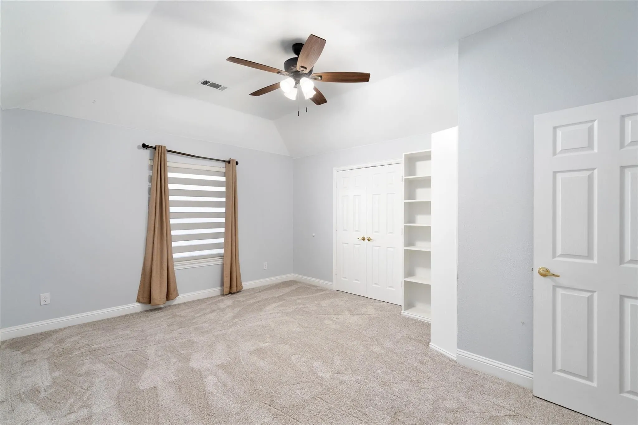 Tray ceiling with a ceiling fan, plush carpeting, built-in shelving, and white paneled doors