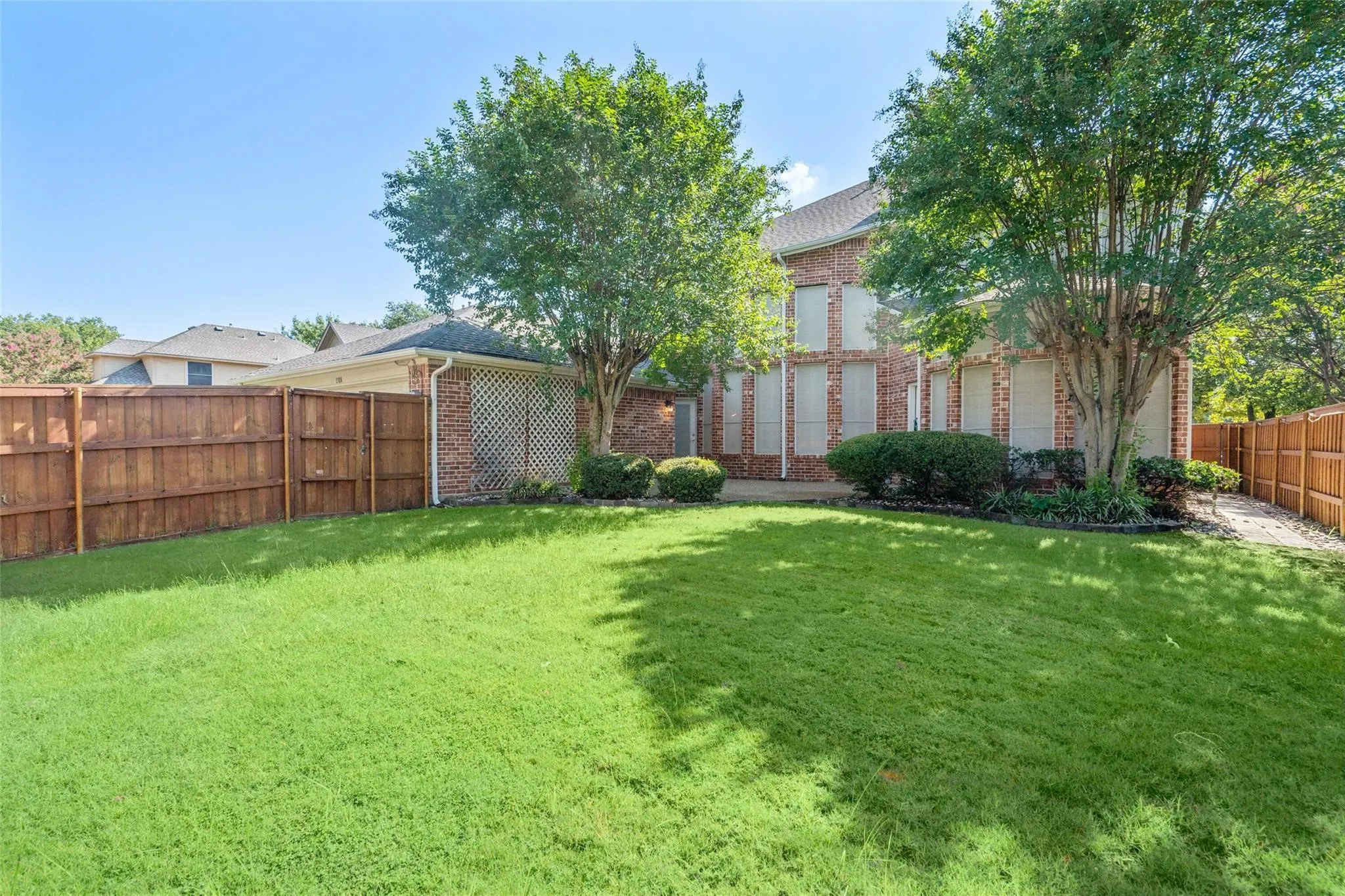 Brick exterior, two-story residence, mature trees, wood privacy fencing, and a manicured lawn