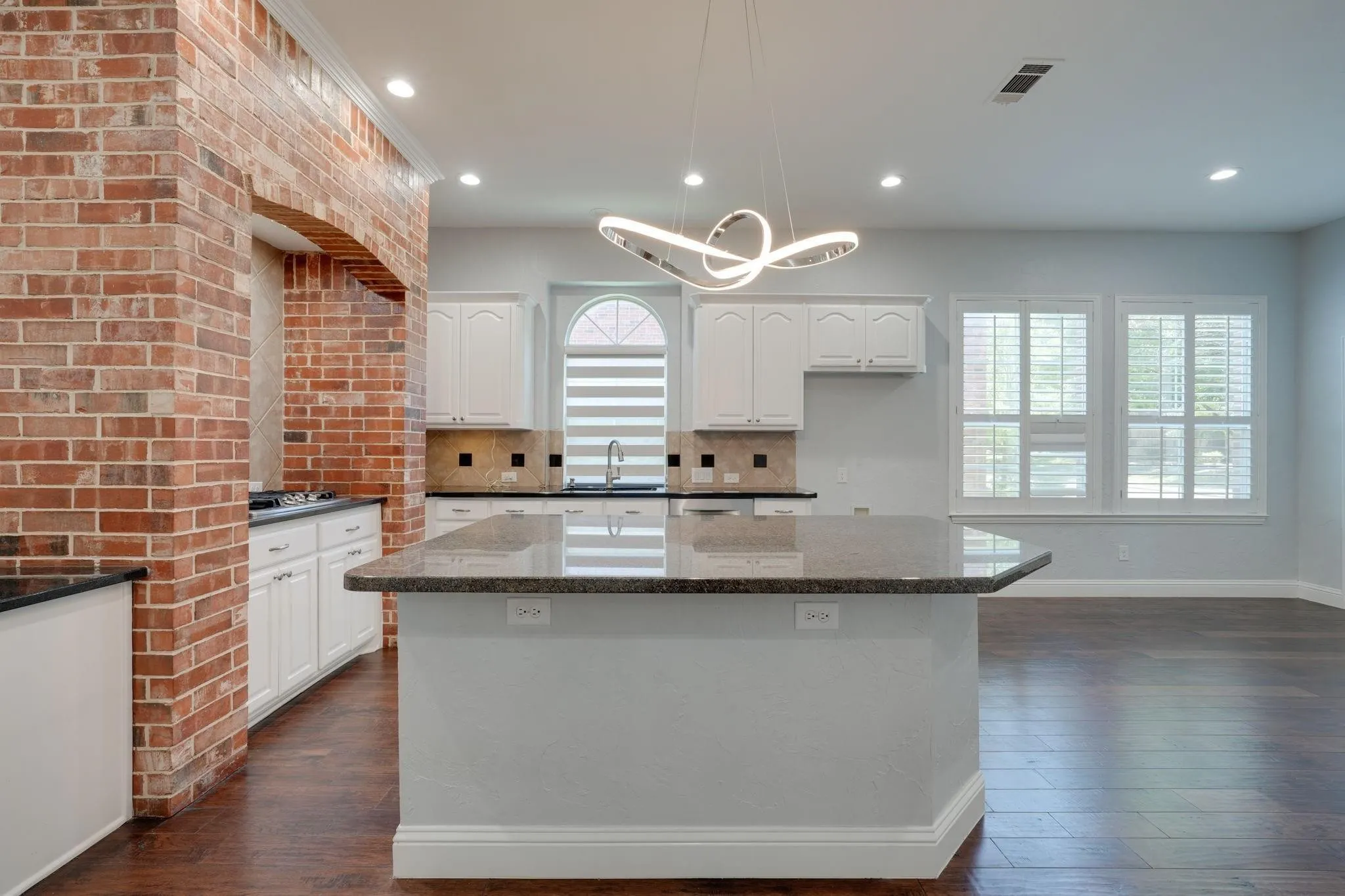 Kitchen island with stone-finish countertop, recessed lighting, and wood-finish flooring