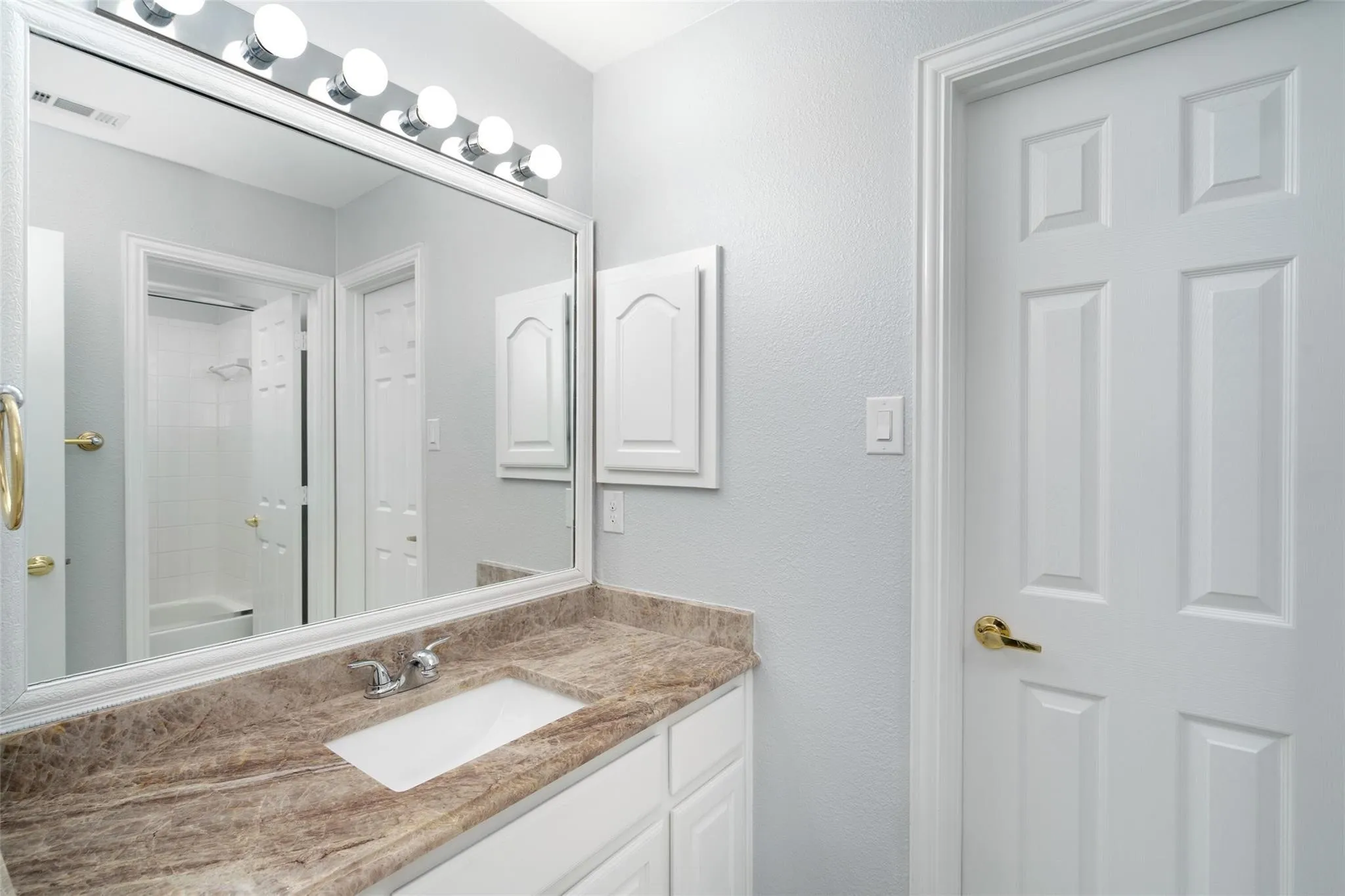 Vanity with a tan patterned countertop and an integrated white sink, complemented by white cabinetry