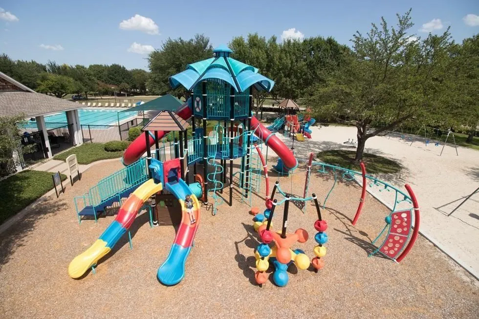Community playground featuring multiple slides, climbing structures, swings, and a shaded seating area