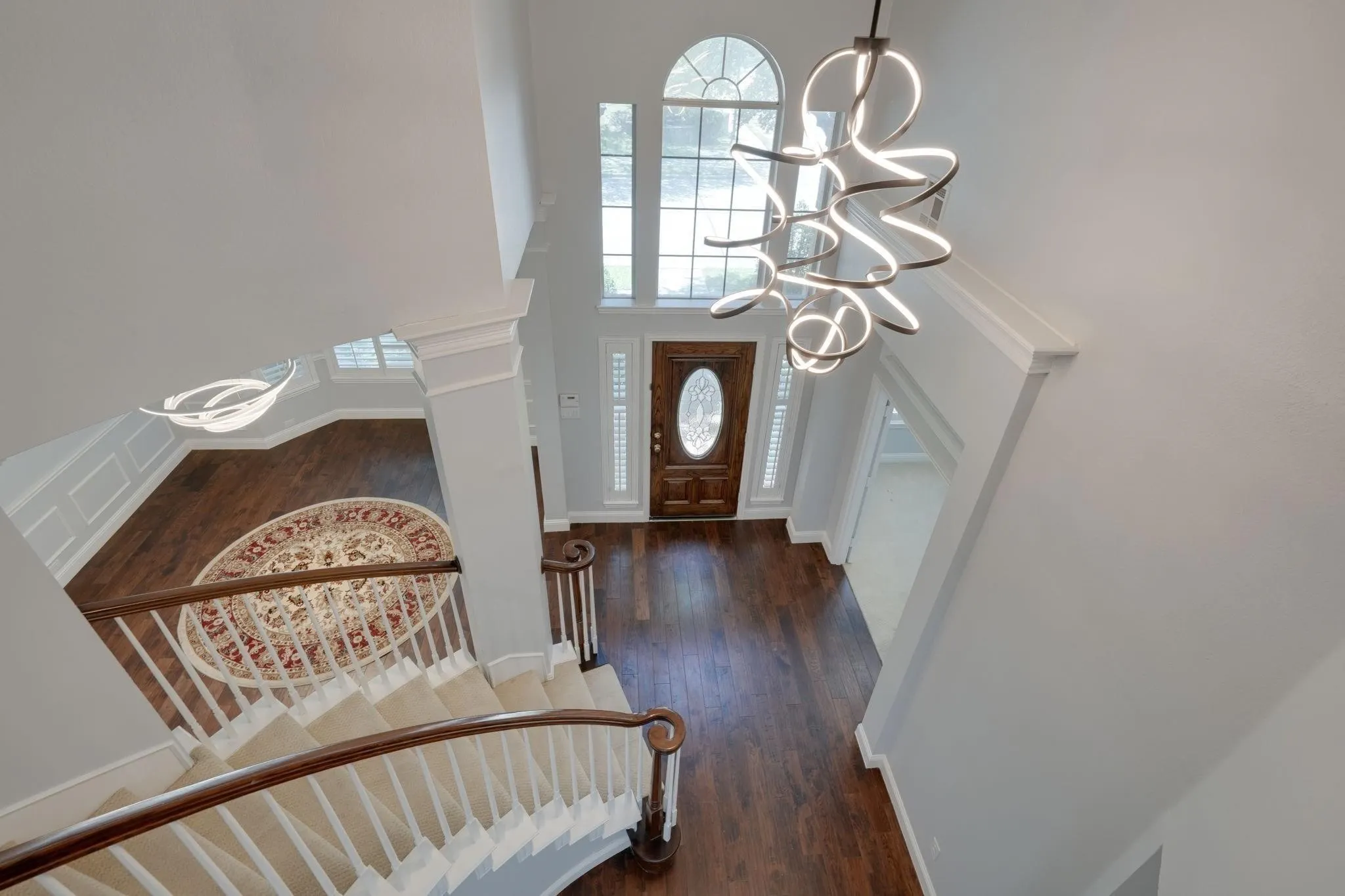 Two-story entryway with a decorative wooden door, arched transom window, and contemporary chandelier
