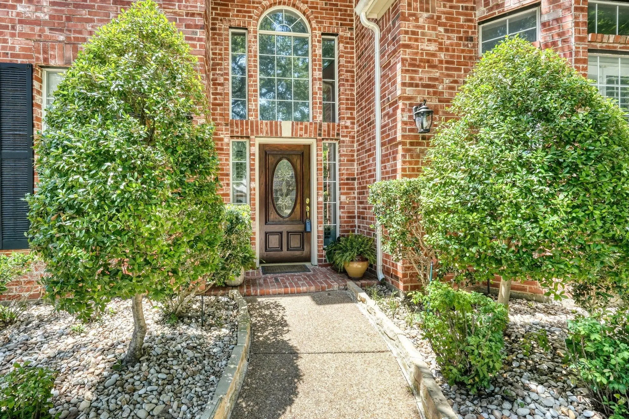 Brick facade with an arched window, decorative front door with an oval glass insert, and a paved walkway bordered by landscaping