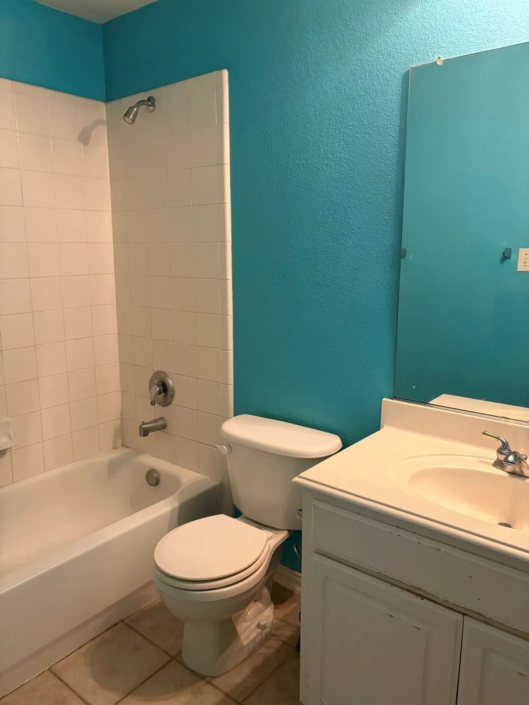 White tile shower surround, white bathtub, white toilet, single vanity with integrated sink, and wall-mounted mirror