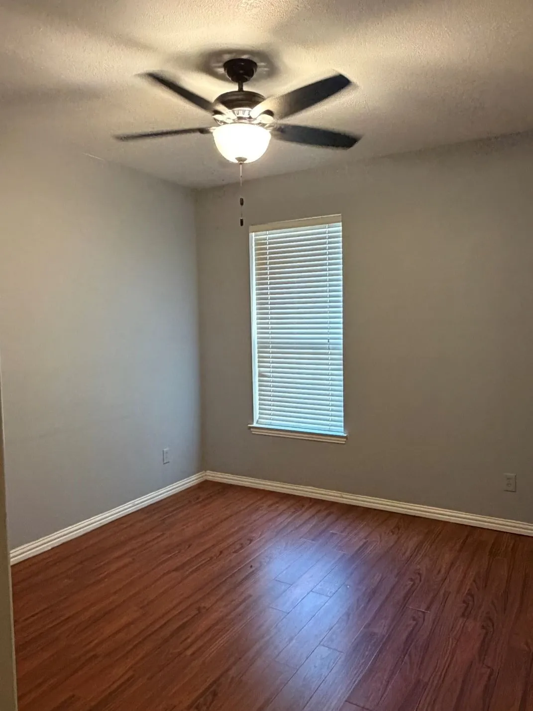 Wood-finish flooring, ceiling fan with integrated lighting, window with horizontal blinds, and neutral wall tones