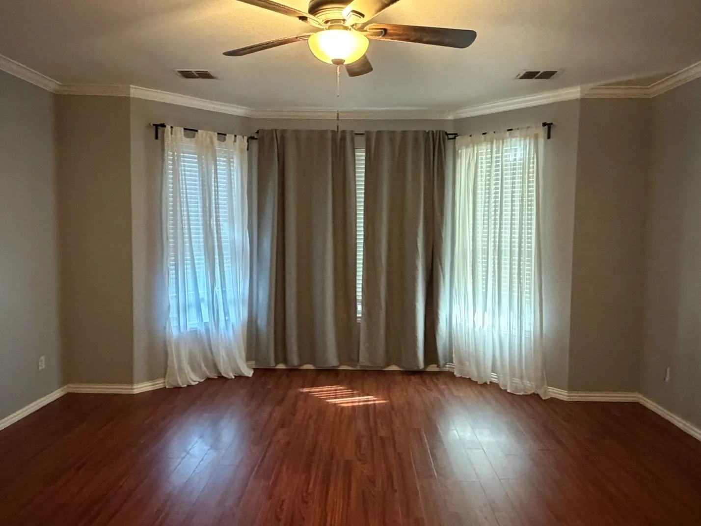 Bay window with multiple windows, wood-finish flooring, crown molding, and a ceiling fan with integrated lighting