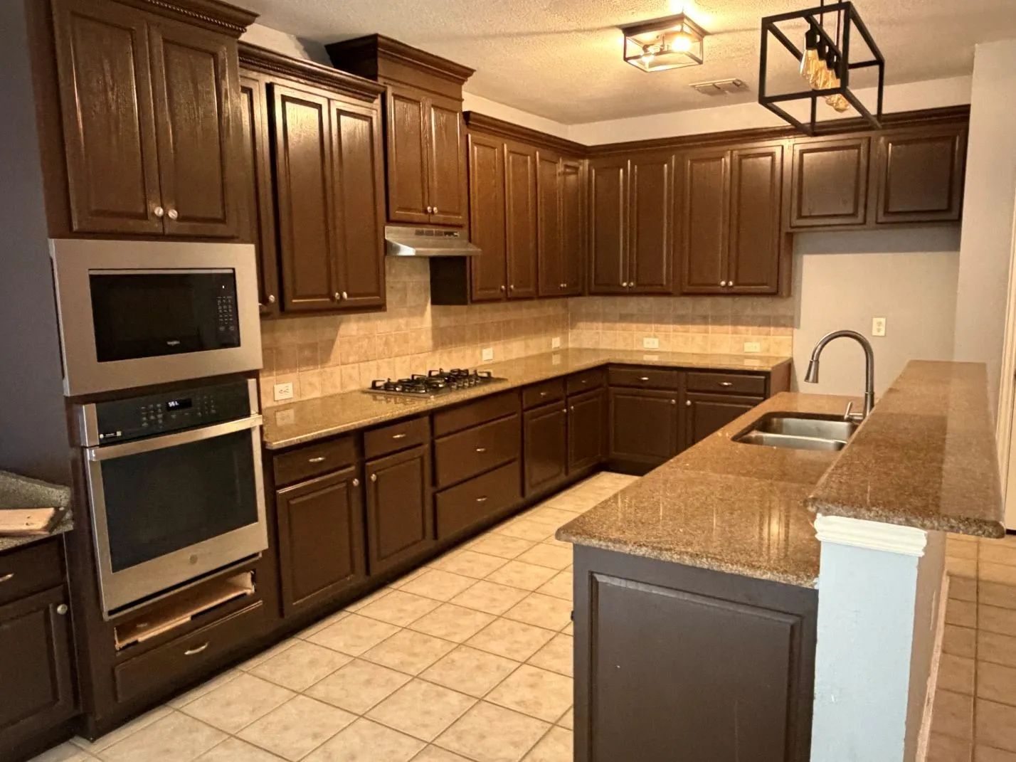 Kitchen featuring dark wood cabinetry, light-toned tiled flooring, stone countertops, stainless steel appliances, and a tiled backsplash