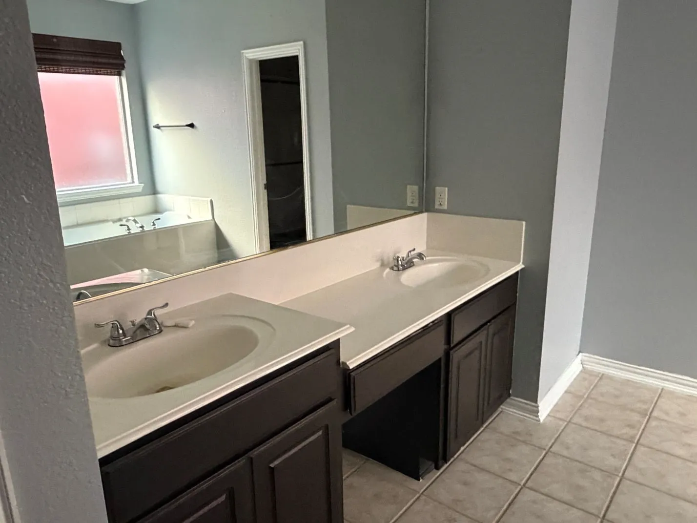 Dual vanity with dark wood-finish cabinetry, solid surface countertops, and tile flooring