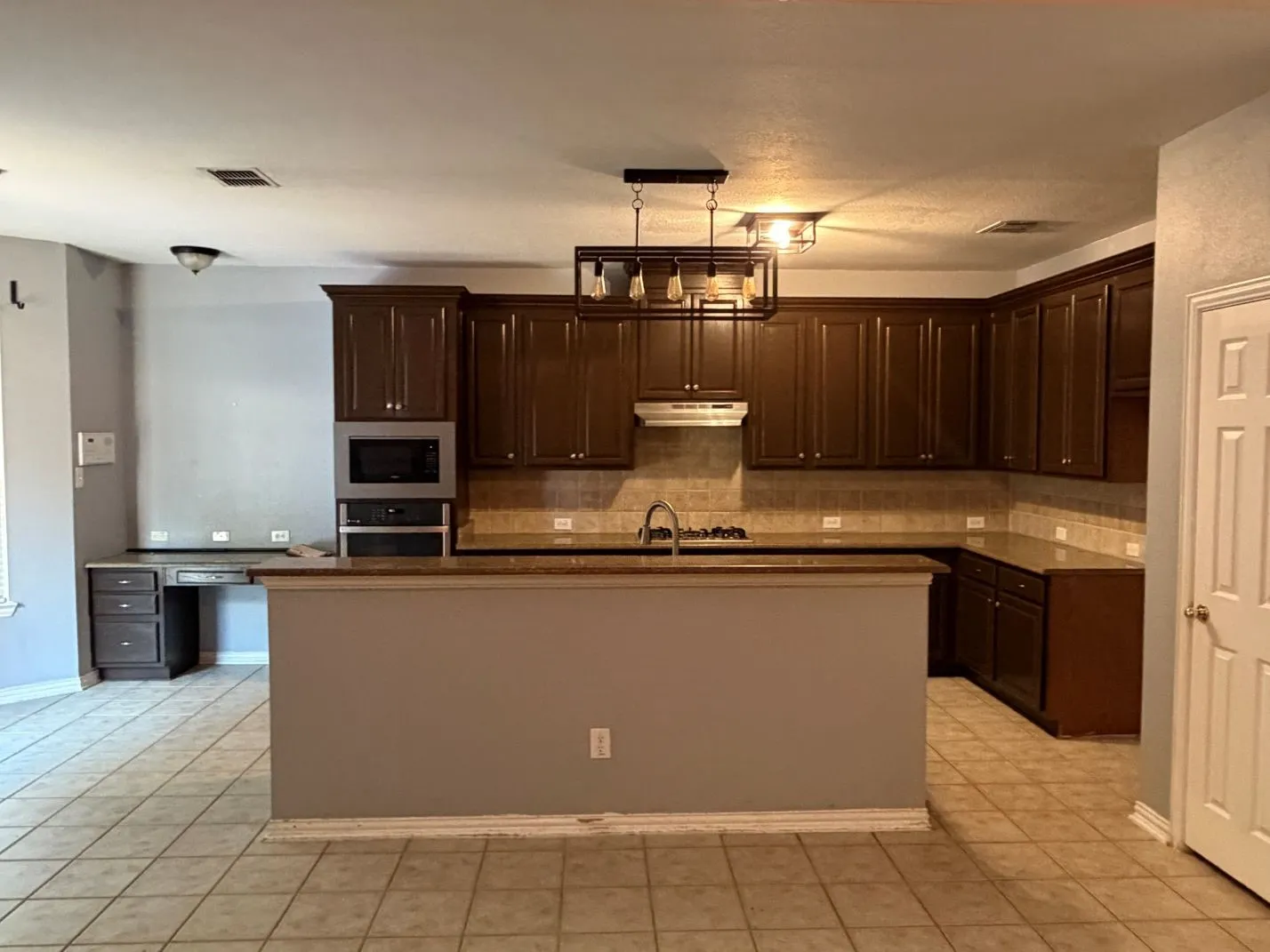 Kitchen featuring dark wood cabinetry, a built-in microwave, integrated oven, and a peninsula with a sink