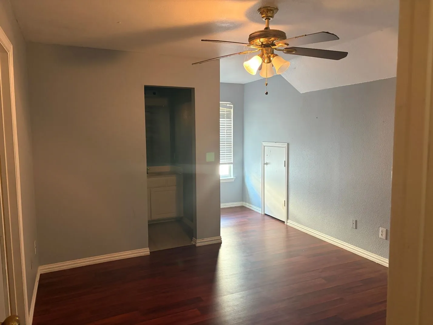 Wood-finish flooring, vaulted ceiling, ceiling fan with light fixture, window with blinds, and white trim