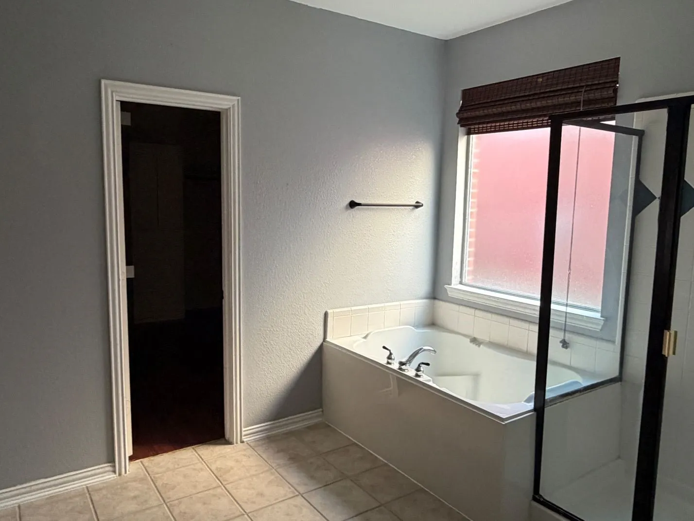 Built-in soaking tub, separate shower enclosure with dark framing, tiled flooring, and a window with blinds