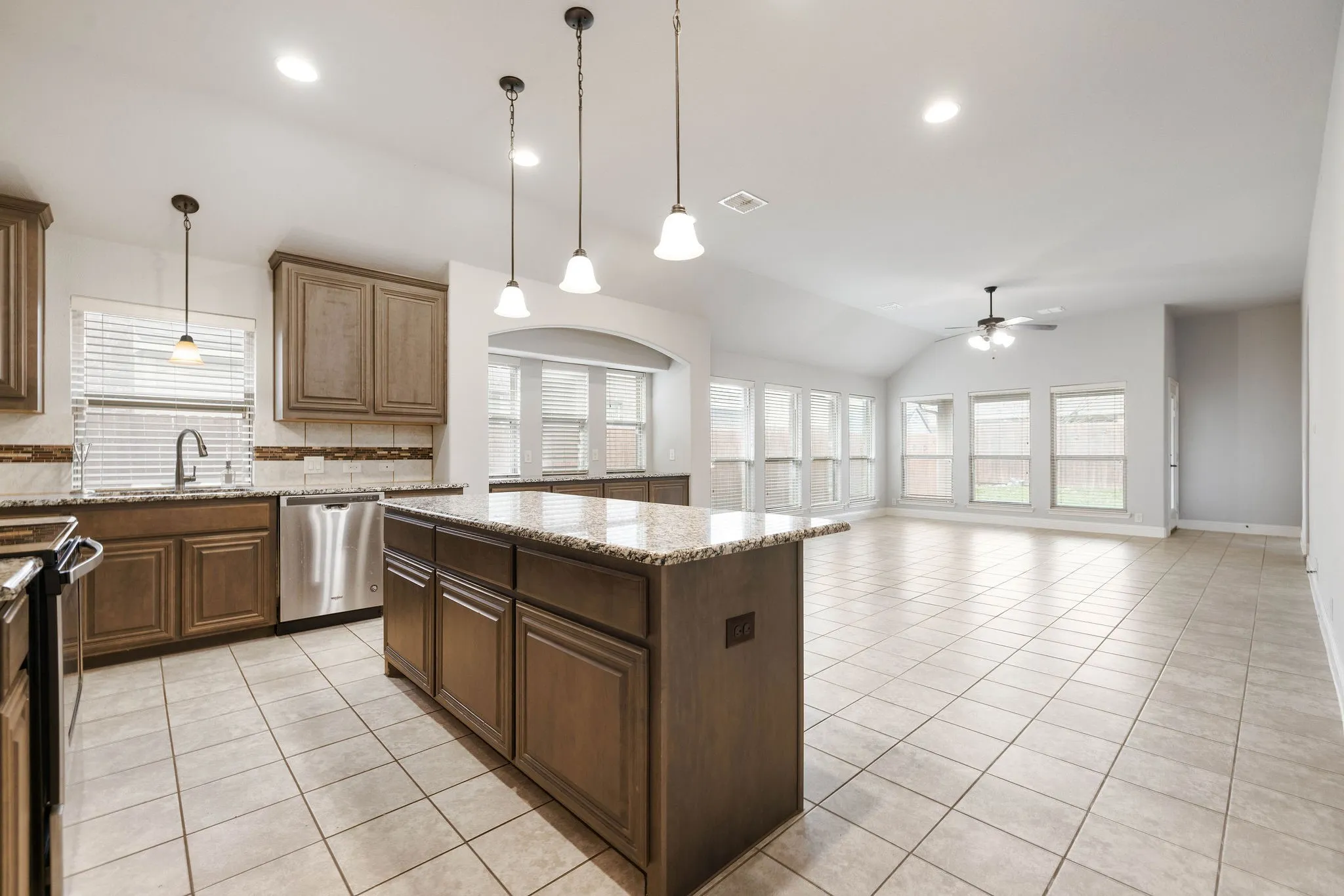 Kitchen featuring pendant lighting, dishwasher, a center island, light stone countertops, and light tile patterned flooring