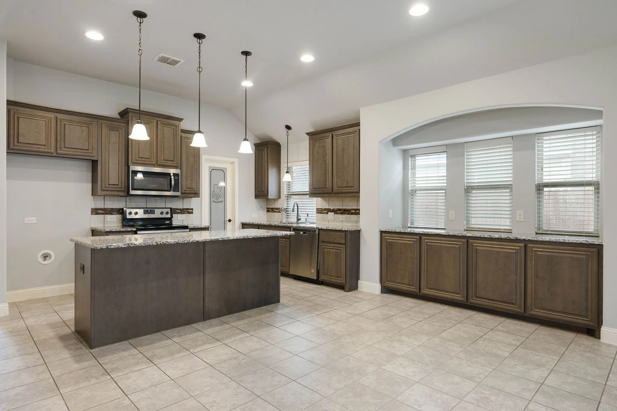 Kitchen with appliances with stainless steel finishes, hanging light fixtures, a center island, light stone counters, and vaulted ceiling