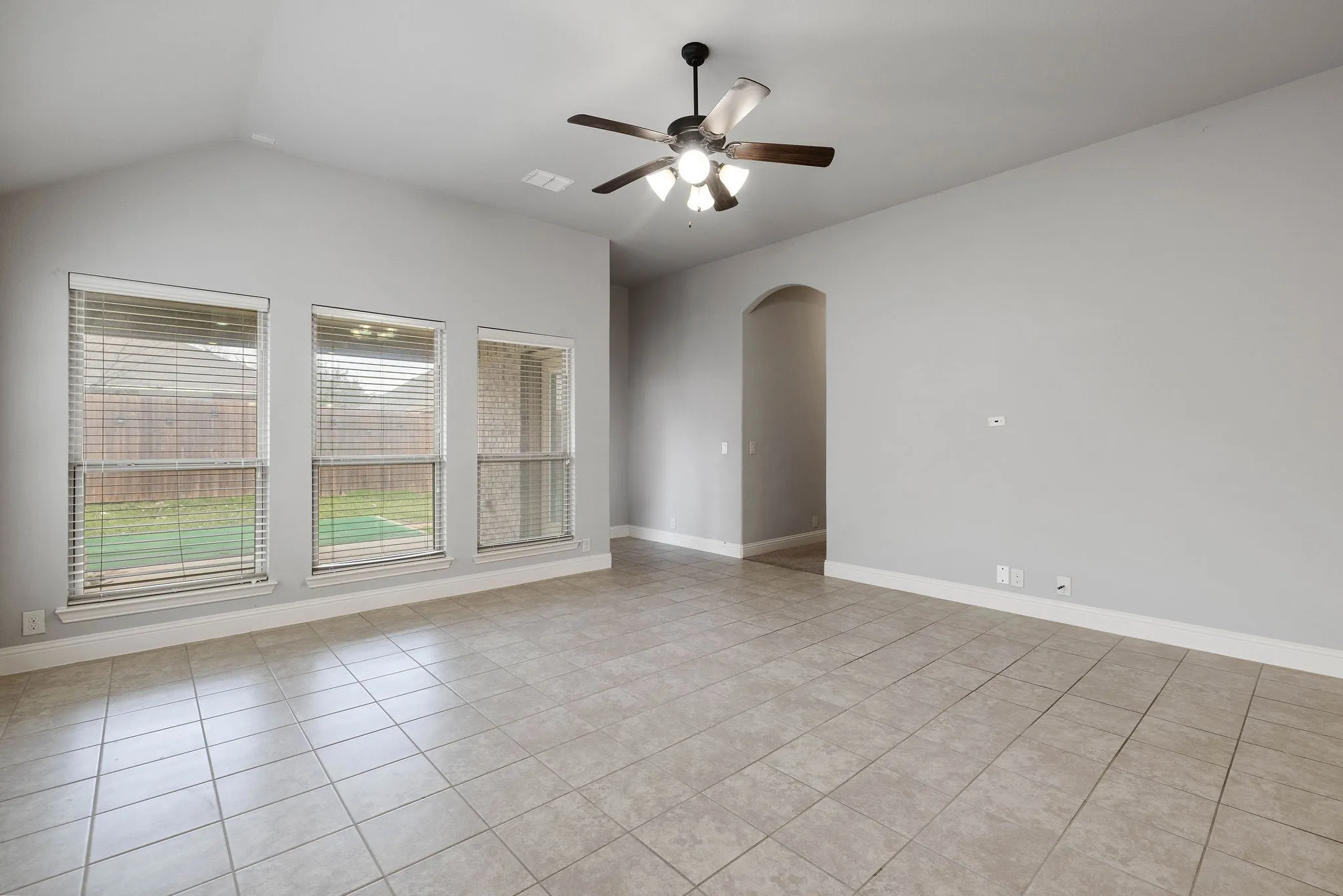 Tiled empty room featuring ceiling fan and vaulted ceiling