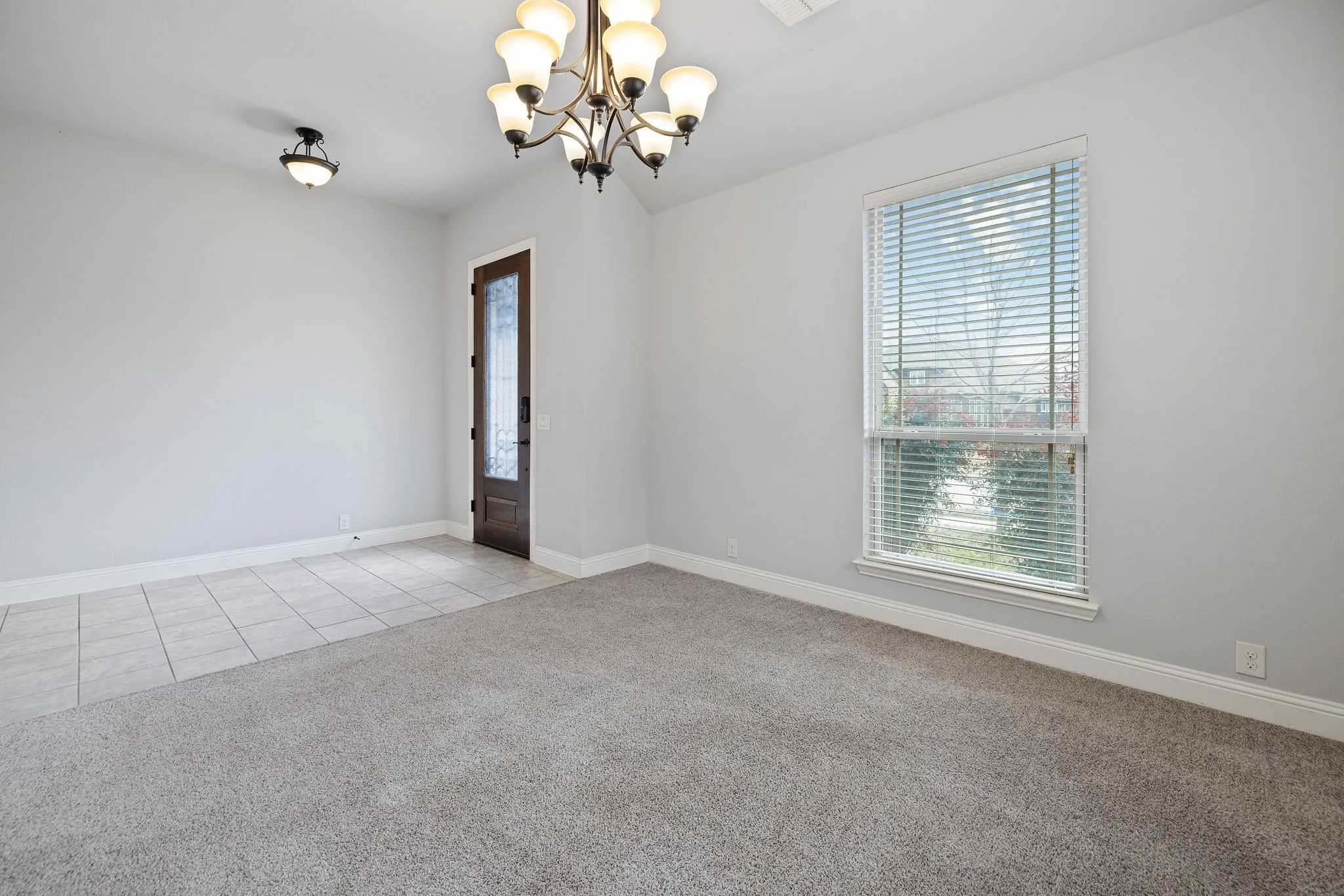 Carpeted front flex room featuring a notable chandelier