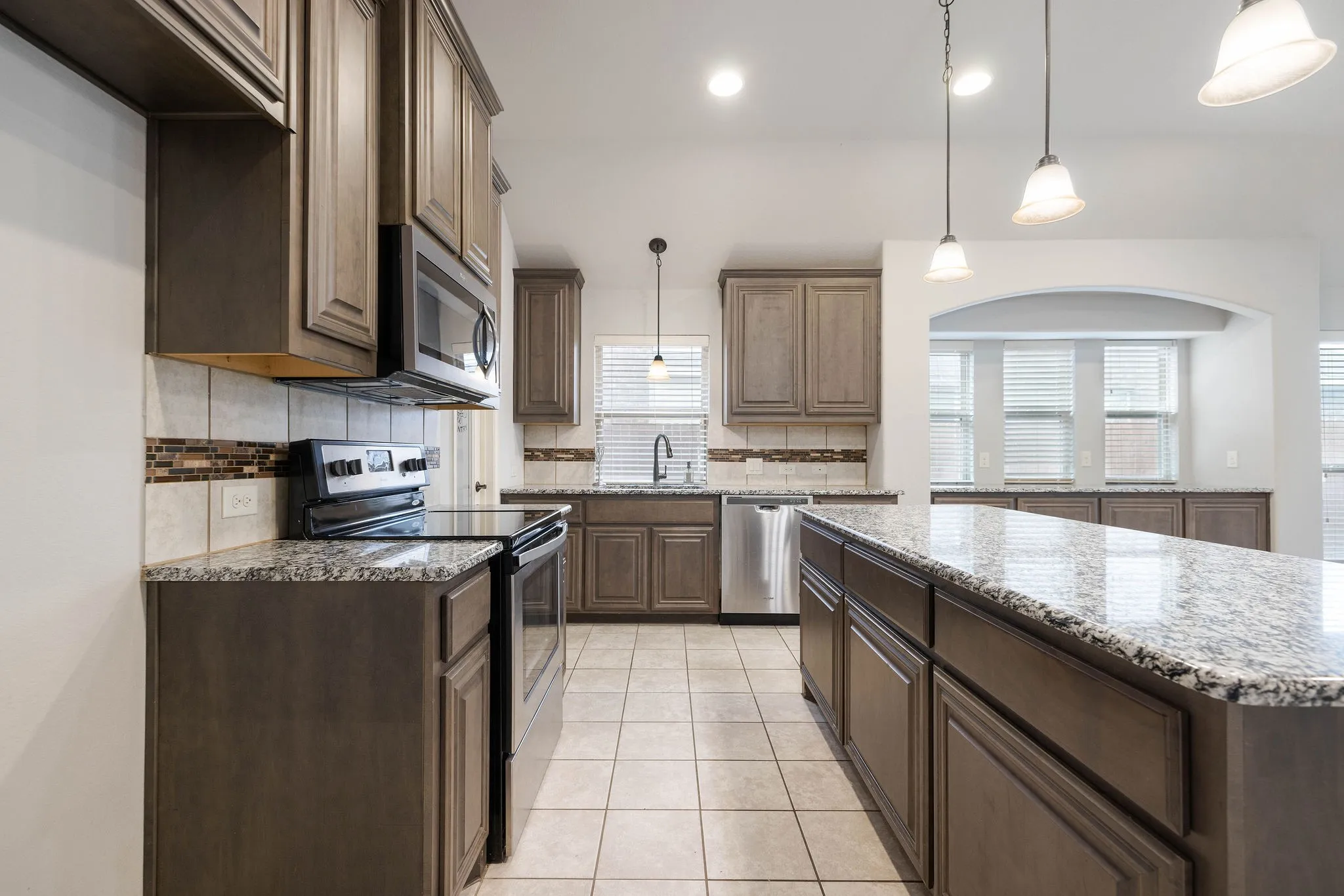 Kitchen featuring pendant lighting, sink, stainless steel appliances, light stone countertops, and a kitchen island