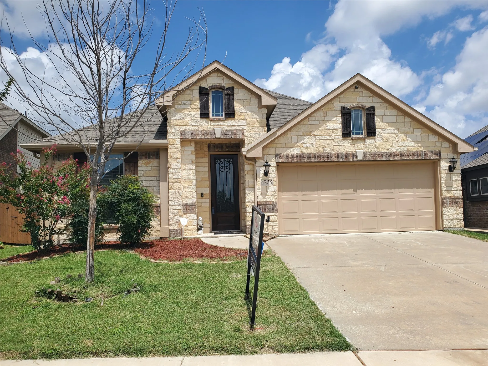 French provincial home featuring stone siding, driveway, a shingled roof, a front lawn, and a garage