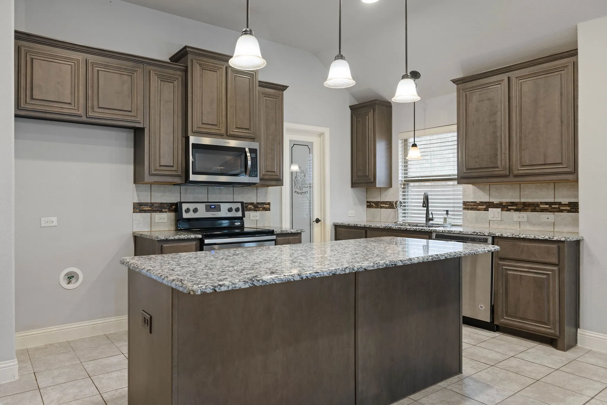 Kitchen with sink, a center island, light tile patterned floors, light stone counters, and stainless steel appliances