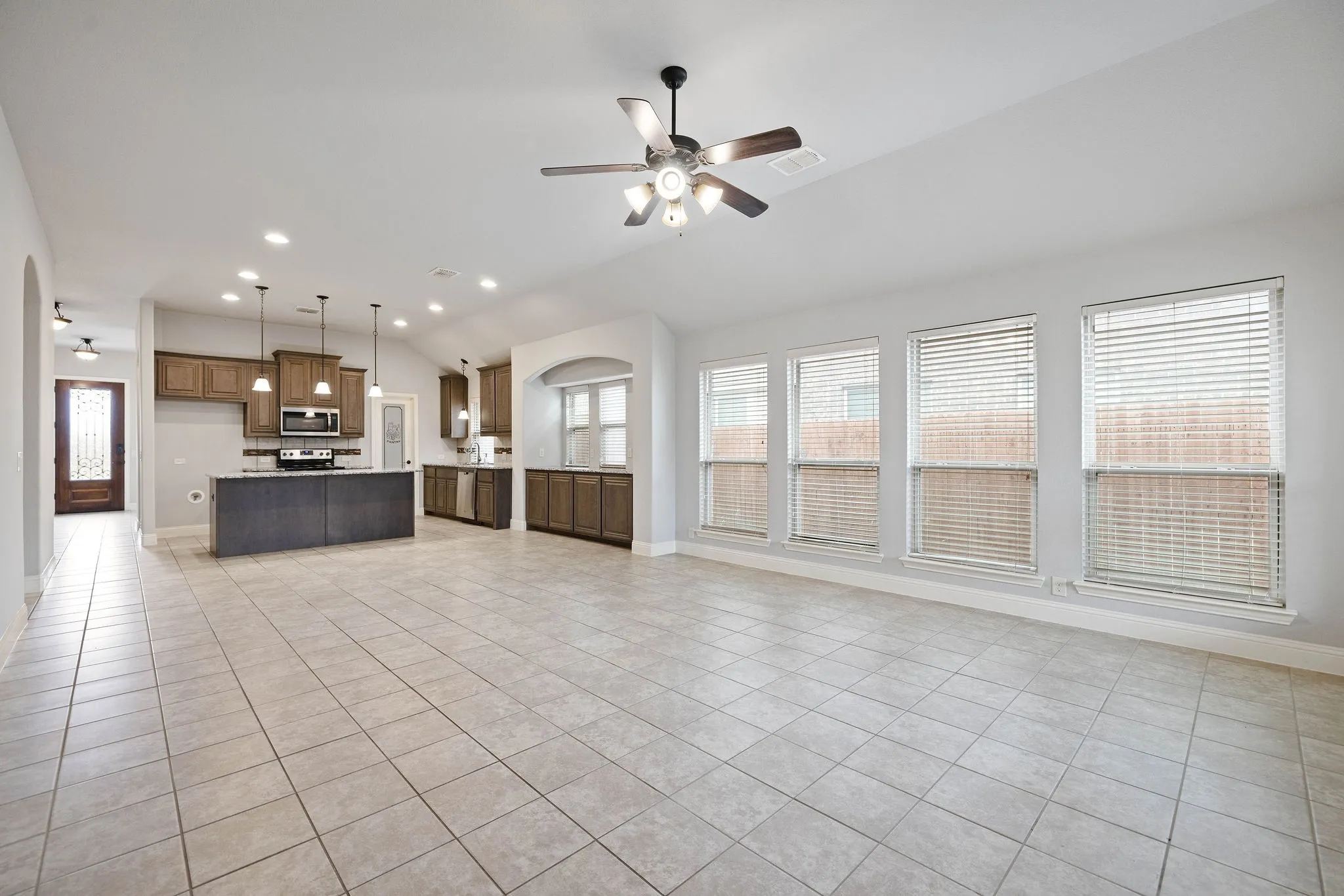 Natural light entering living room with light tile patterned flooring, vaulted ceiling, and ceiling fan