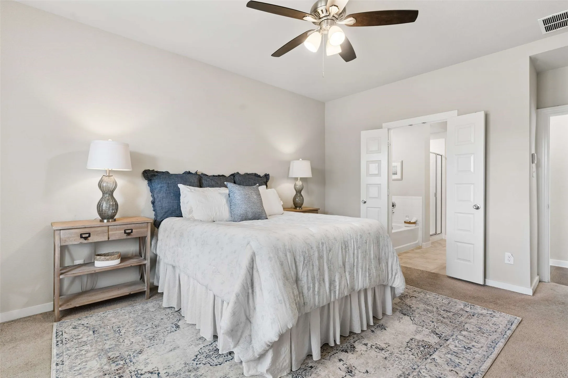 Recessed lighting, ceiling fan, carpeted flooring, white paneled doors, and an en-suite bathroom with a soaking tub and glass-enclosed shower
