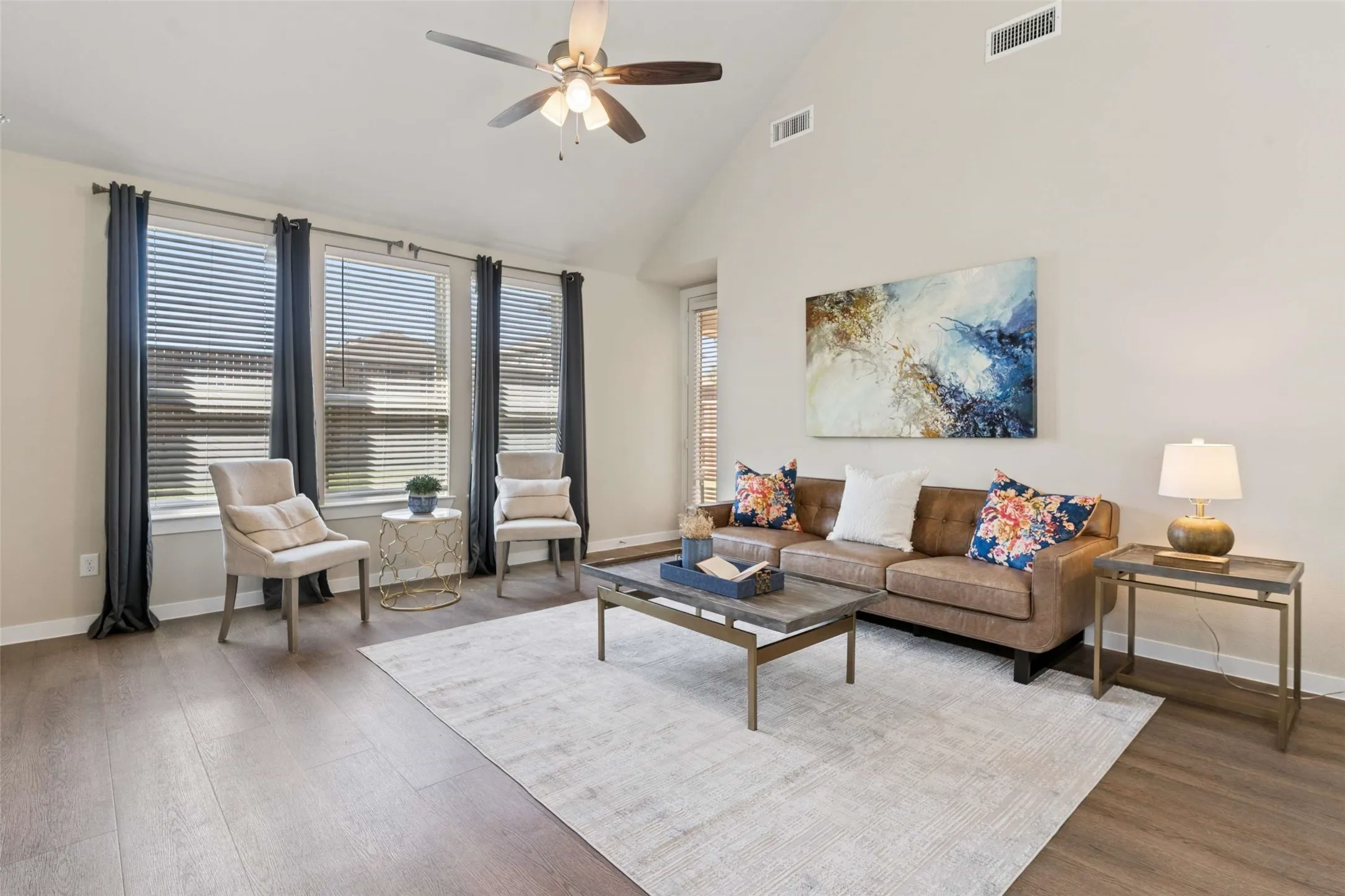 Vaulted ceiling, ceiling fan, wood-finish flooring, multiple windows with blinds, and neutral wall tones