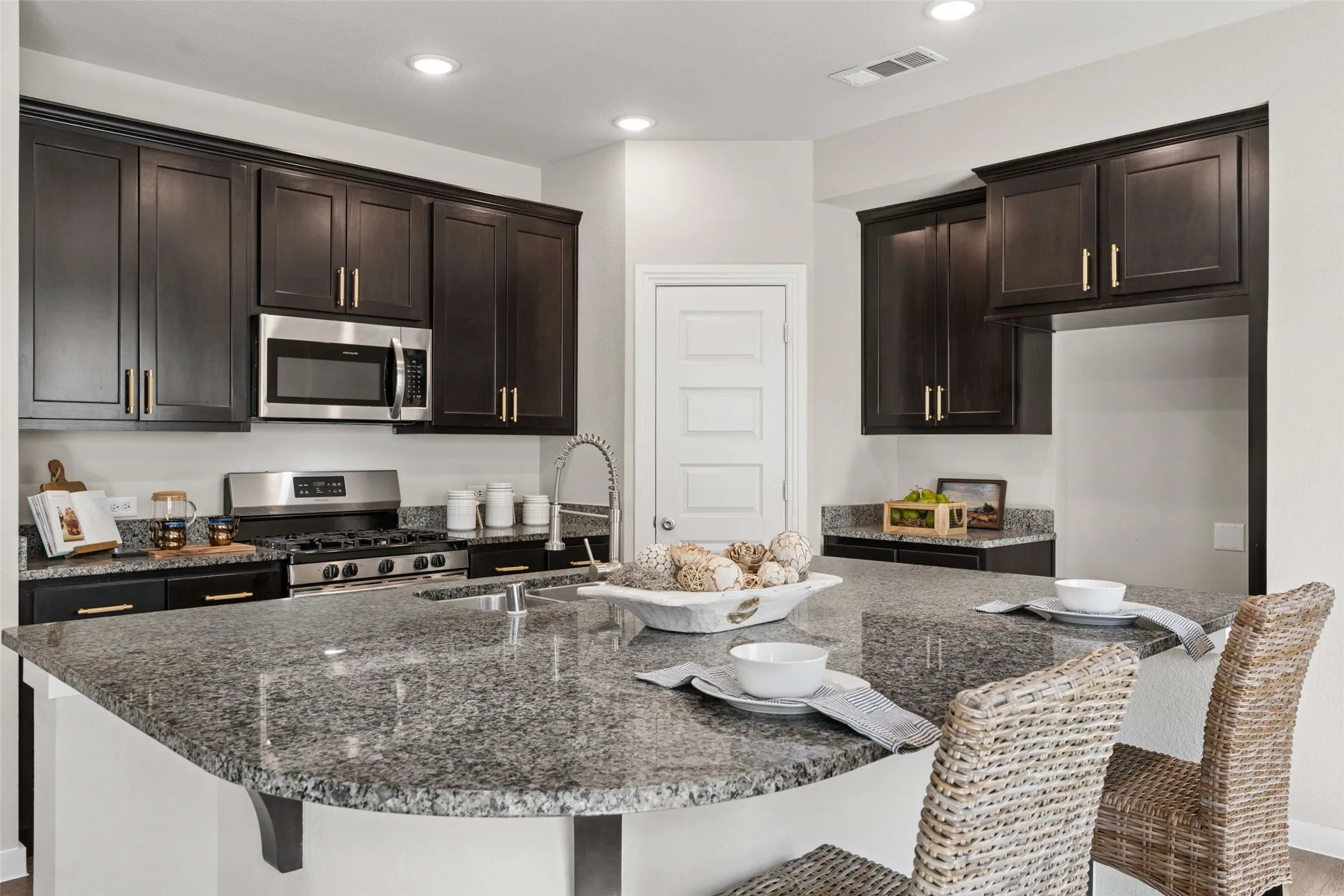 Kitchen featuring dark wood cabinetry, granite countertops, stainless steel appliances, a built-in microwave, and recessed lighting