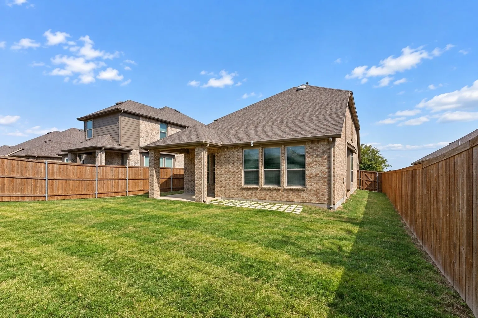 Expansive green lawn, brick exterior, covered patio, privacy fencing, and exterior window trim