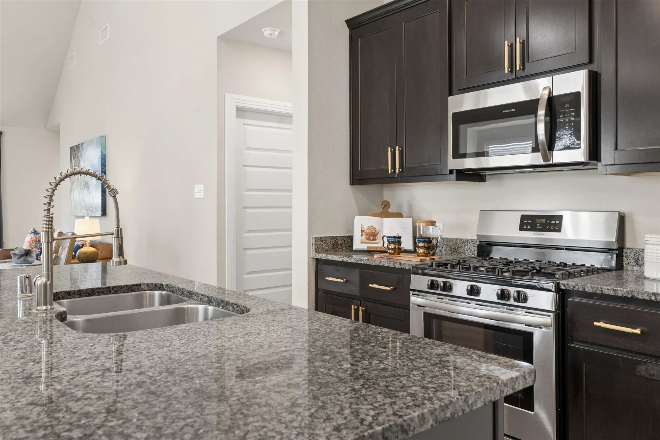 Kitchen featuring dark wood-finish cabinetry, stainless steel appliances, a double basin sink with a gooseneck faucet, and granite countertops