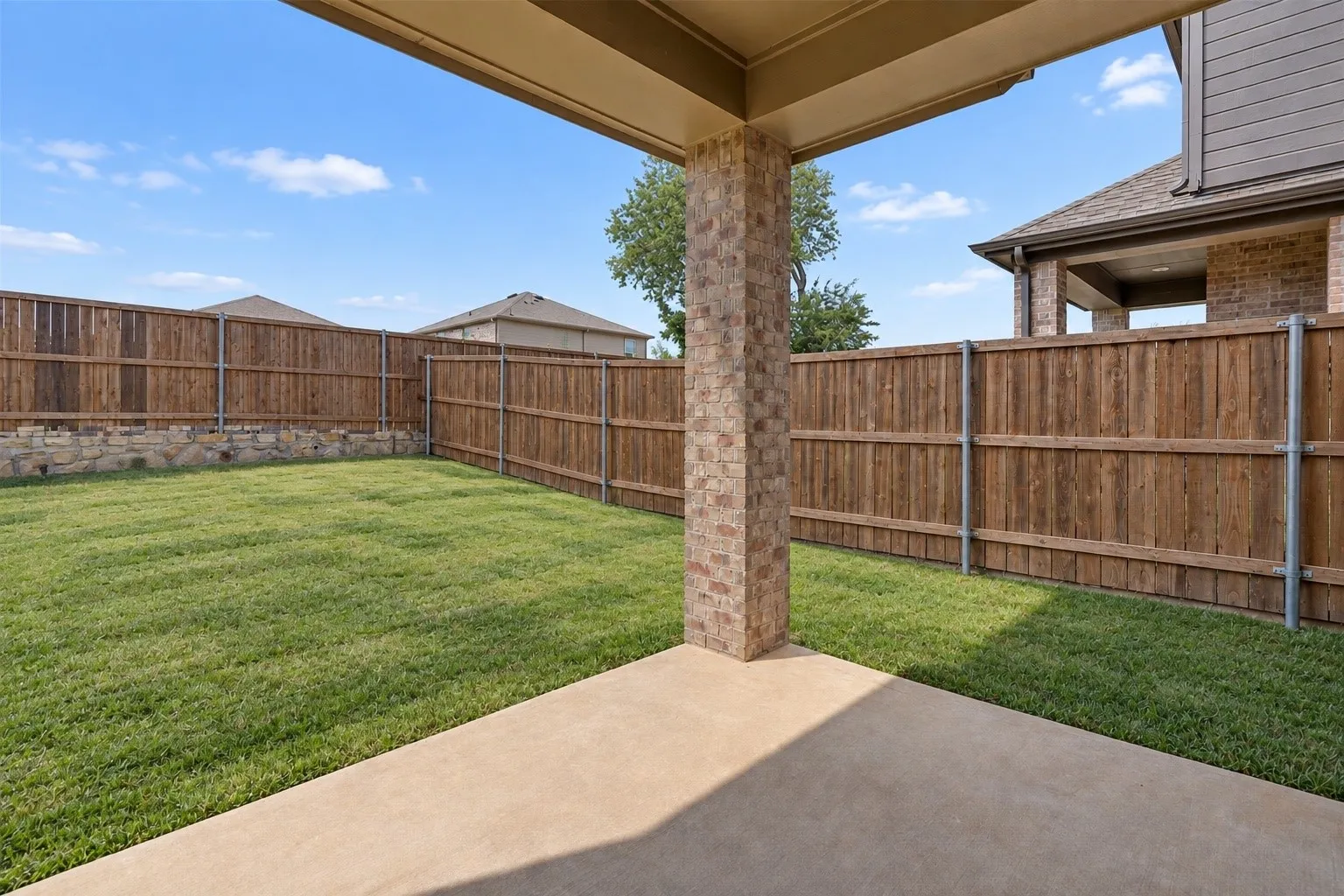 Covered patio with a stone-clad support column, concrete surface, and a spacious grassy yard