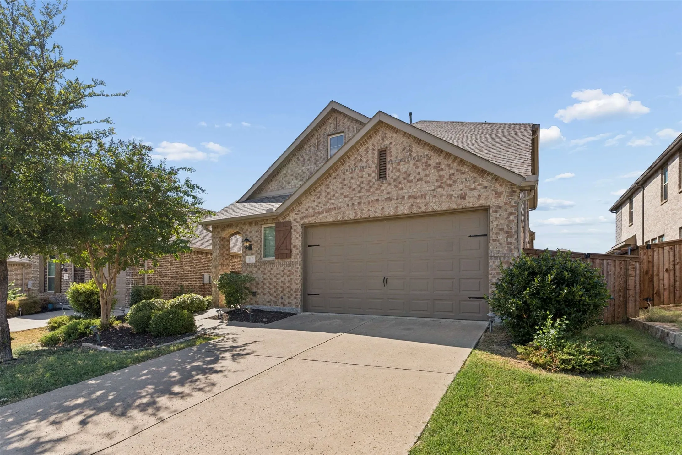 Brick exterior with wood shutters, attached two-car garage, concrete driveway, and established landscaping