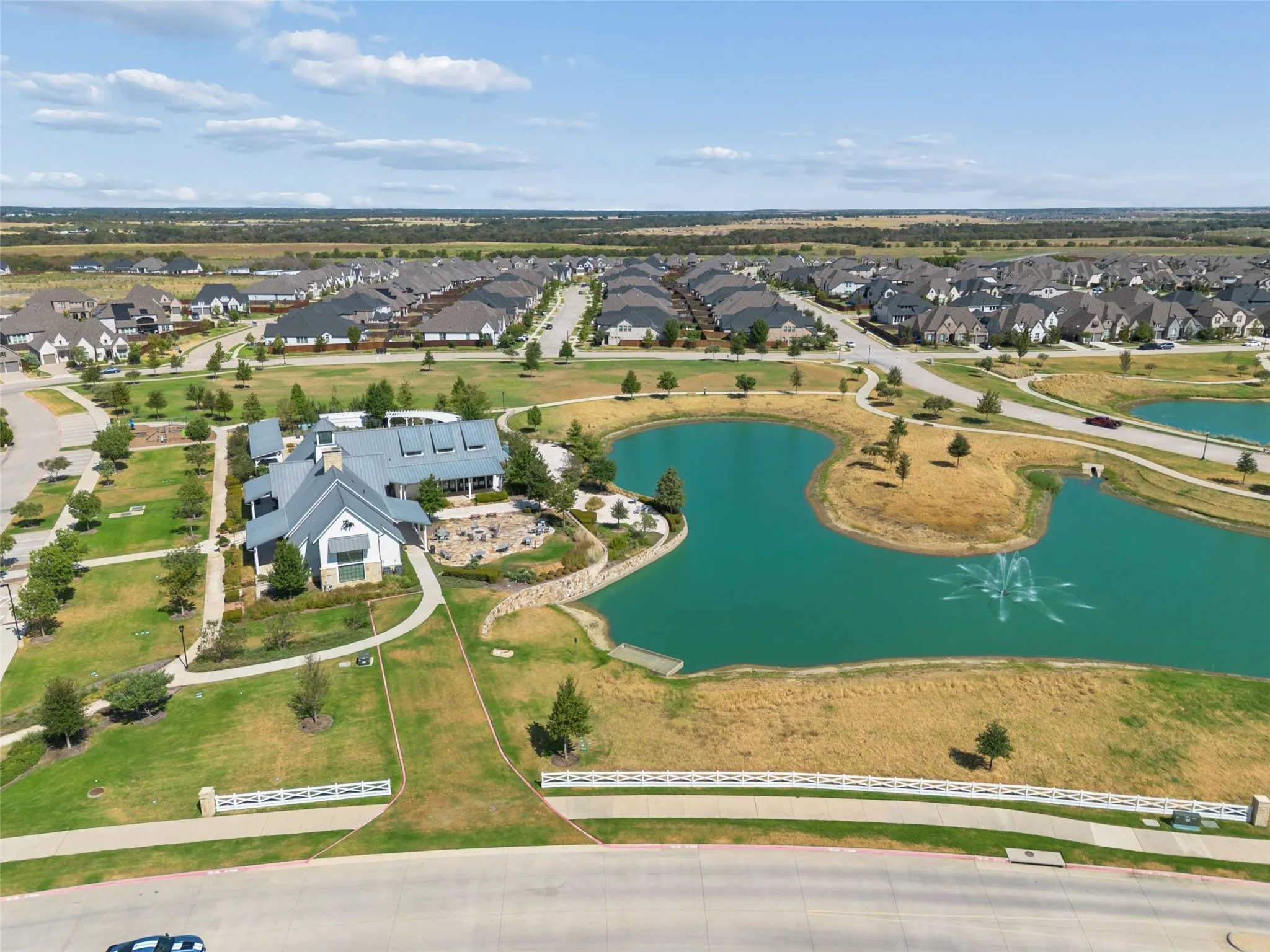 Community grounds featuring a prominent clubhouse, extensive green spaces, and a pond with a water fountain