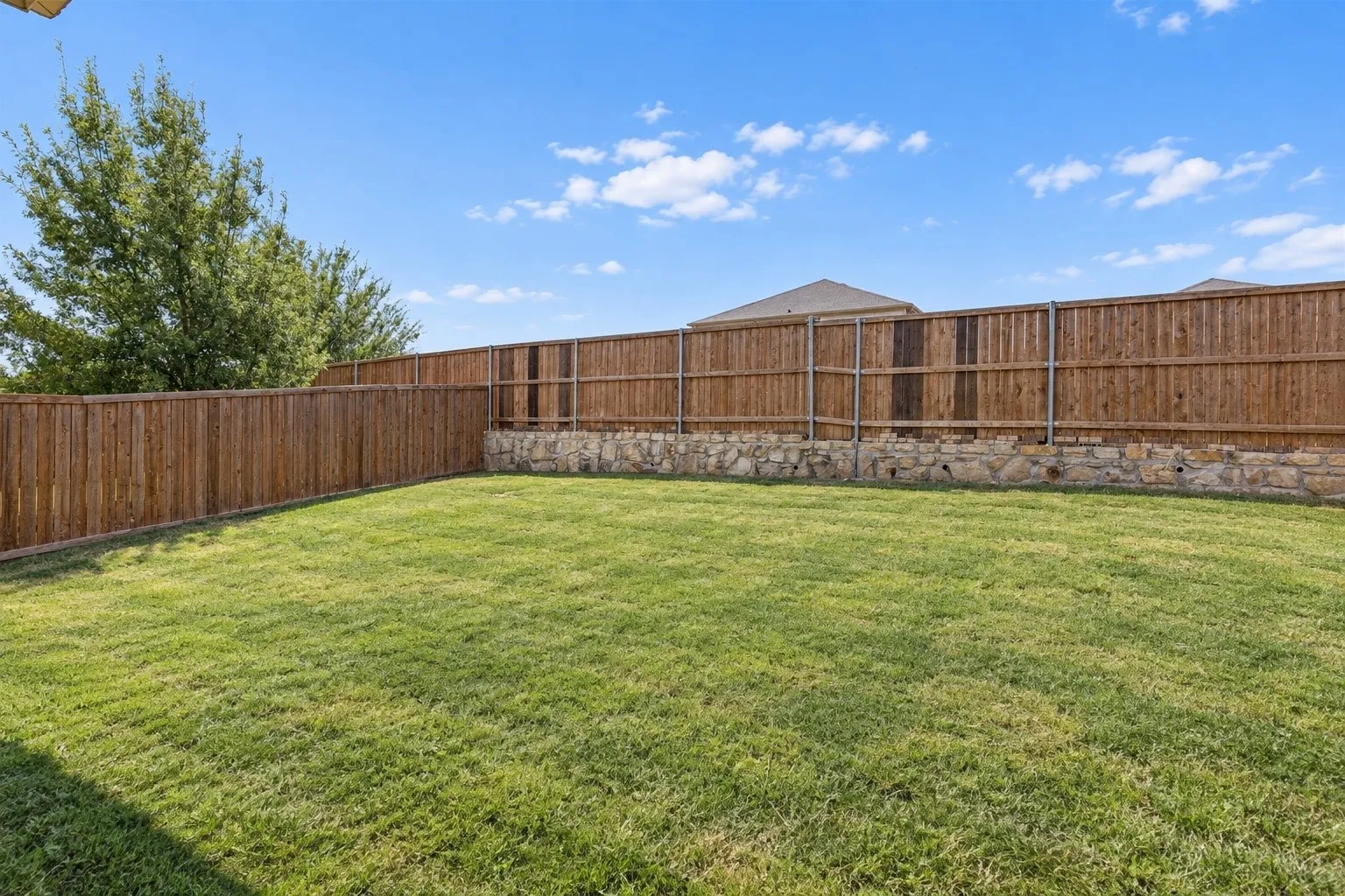 Expansive grassy yard with wood fencing and a stone retaining wall
