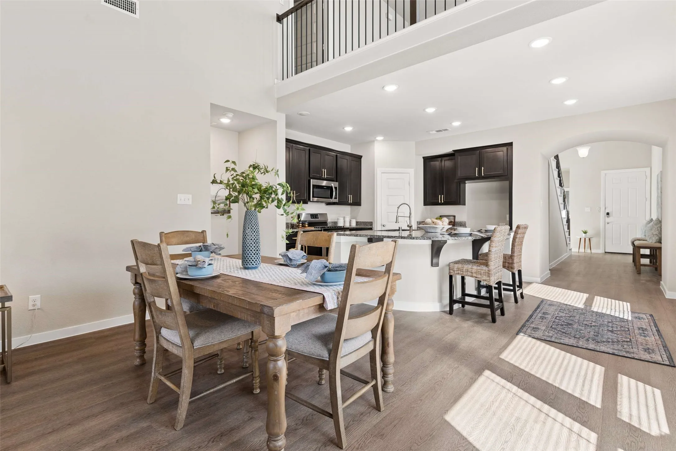 Two-story ceiling, recessed lighting, wood-finish flooring, dark wood cabinetry, and a kitchen island with seating