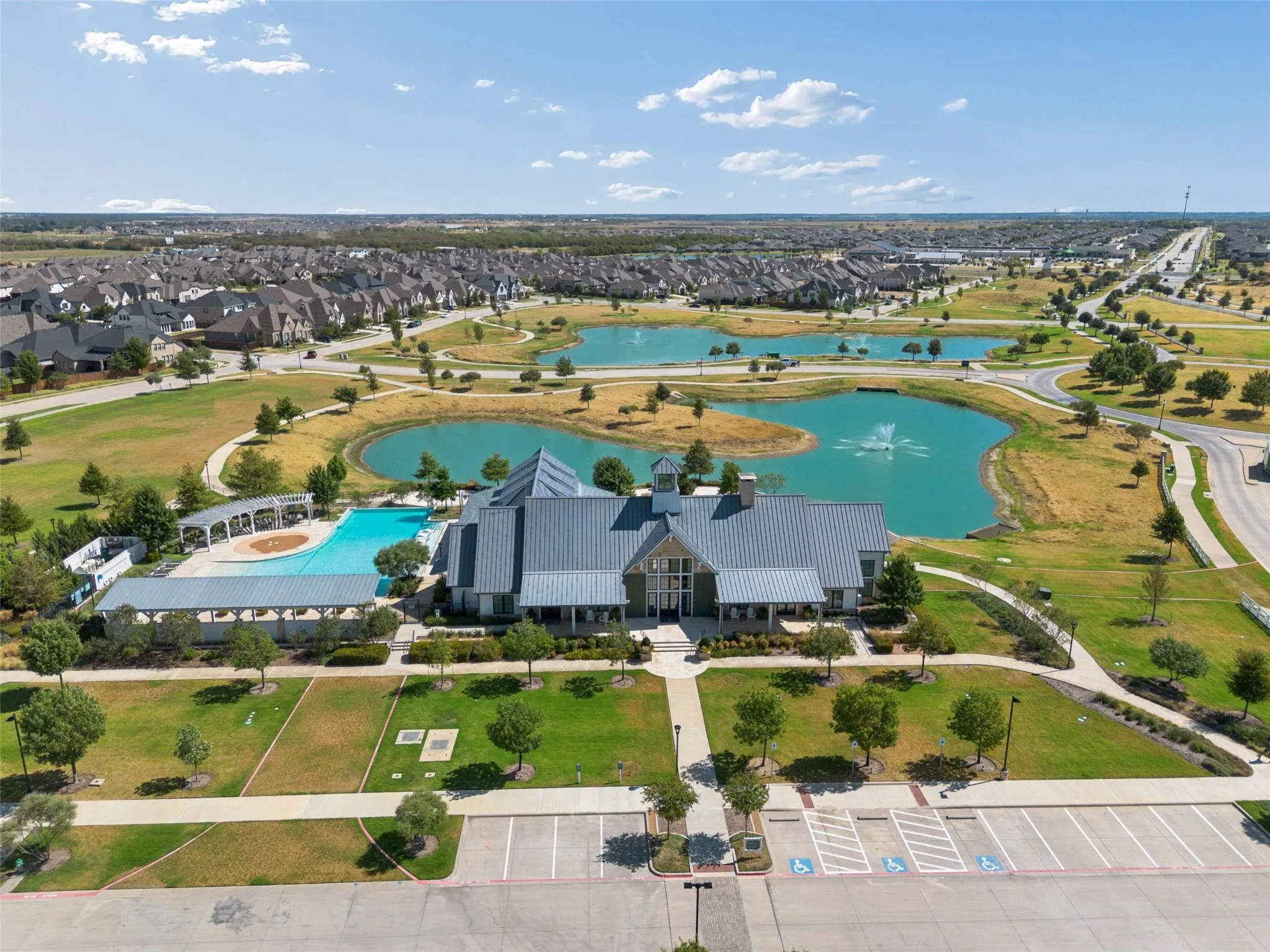 Community clubhouse with a gabled roofline, adjacent swimming pool, and multiple water features